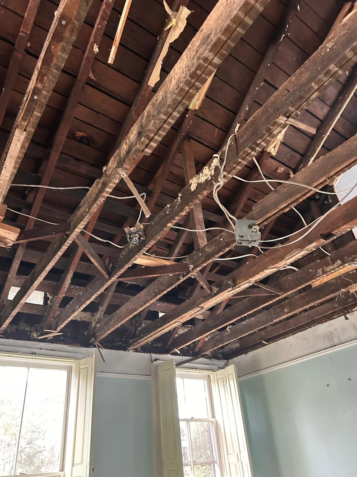 The ceiling of a room with removed drywall showing exposed wooden beams, wires, and electrical boxes.