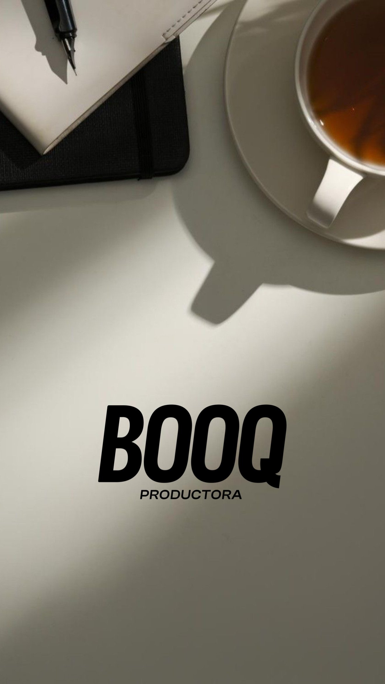 Una taza de café en un plato, una libreta con un bolígrafo, y un libro o cuaderno en una mesa de oficina