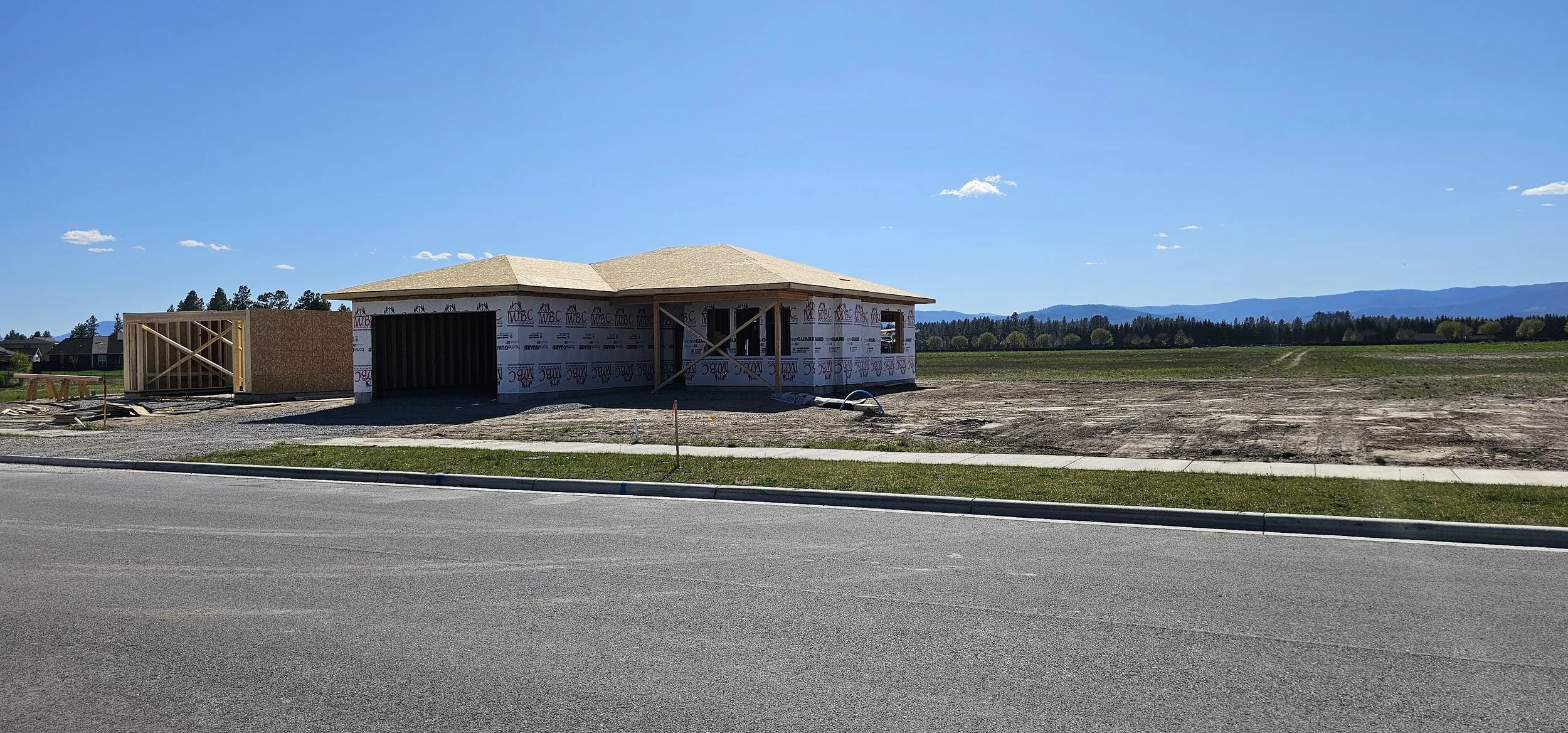 New house under construction on a vacant lot, with a clear blue sky and distant mountains in the background.