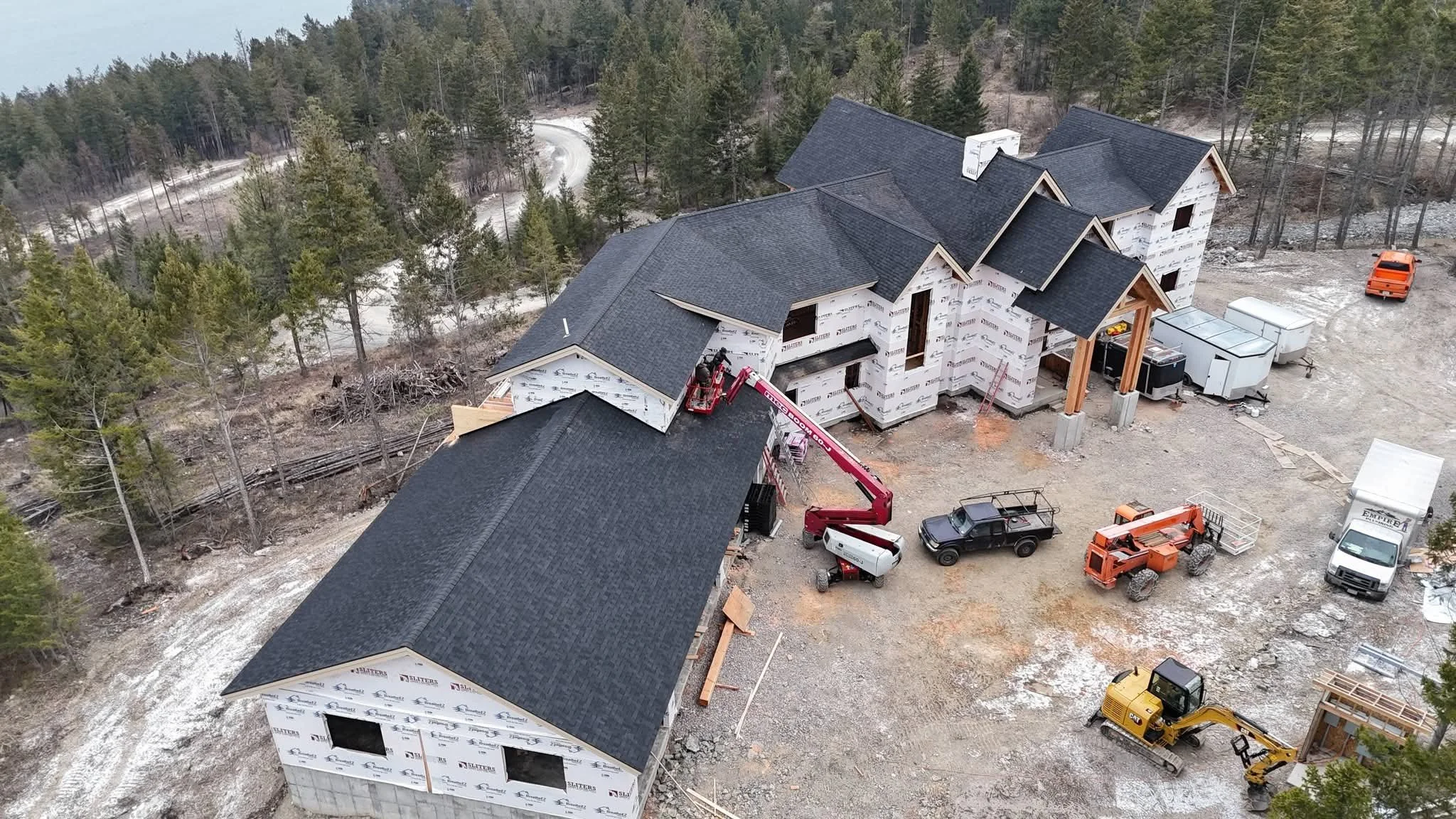 Aerial view of a large house under construction in a wooded area, with construction vehicles and equipment around the site.