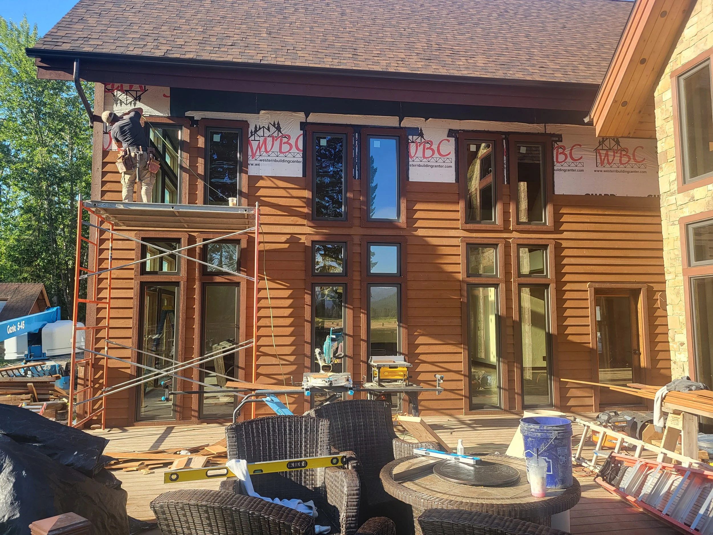 Construction workers installing windows on a wooden house exterior with construction tools and equipment on the deck.