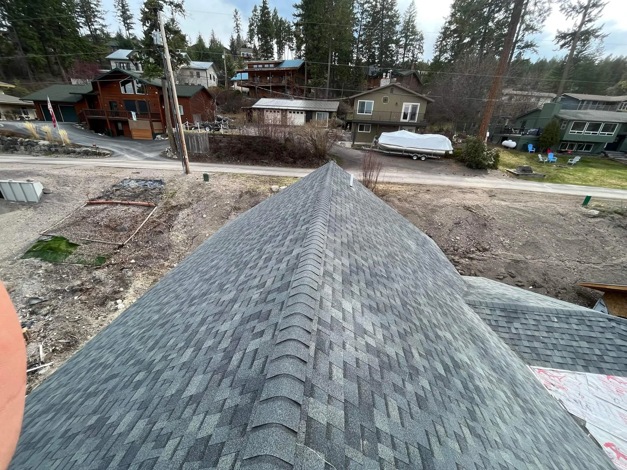 A view from the roof of a building showing a residential neighborhood with multiple houses, trees, and a dirt lot nearby.