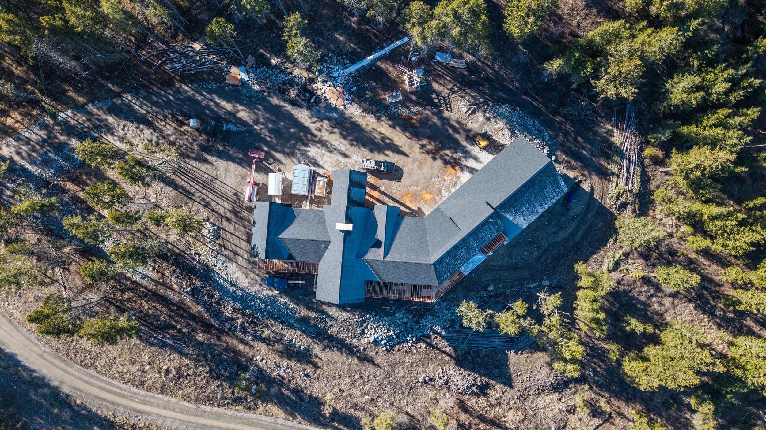 An aerial view of a house surrounded by trees in a forested area, with construction materials and vehicles nearby.
