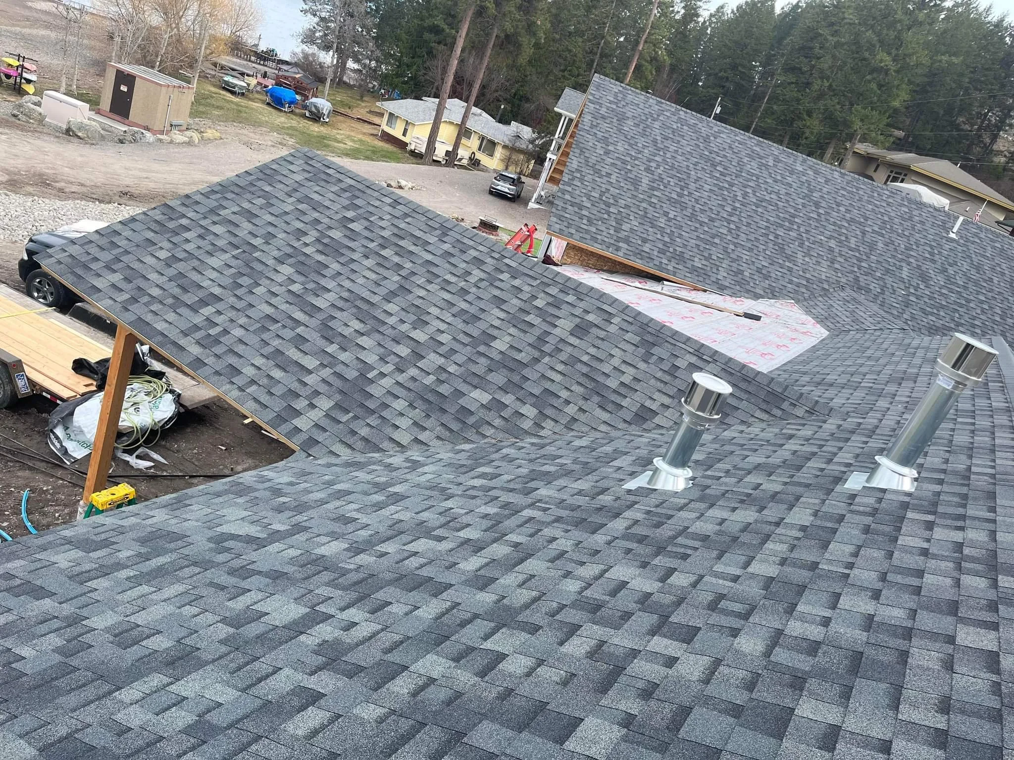 Aerial view of a house roof under construction with gray asphalt shingles, two metal vents, and a partially completed section.