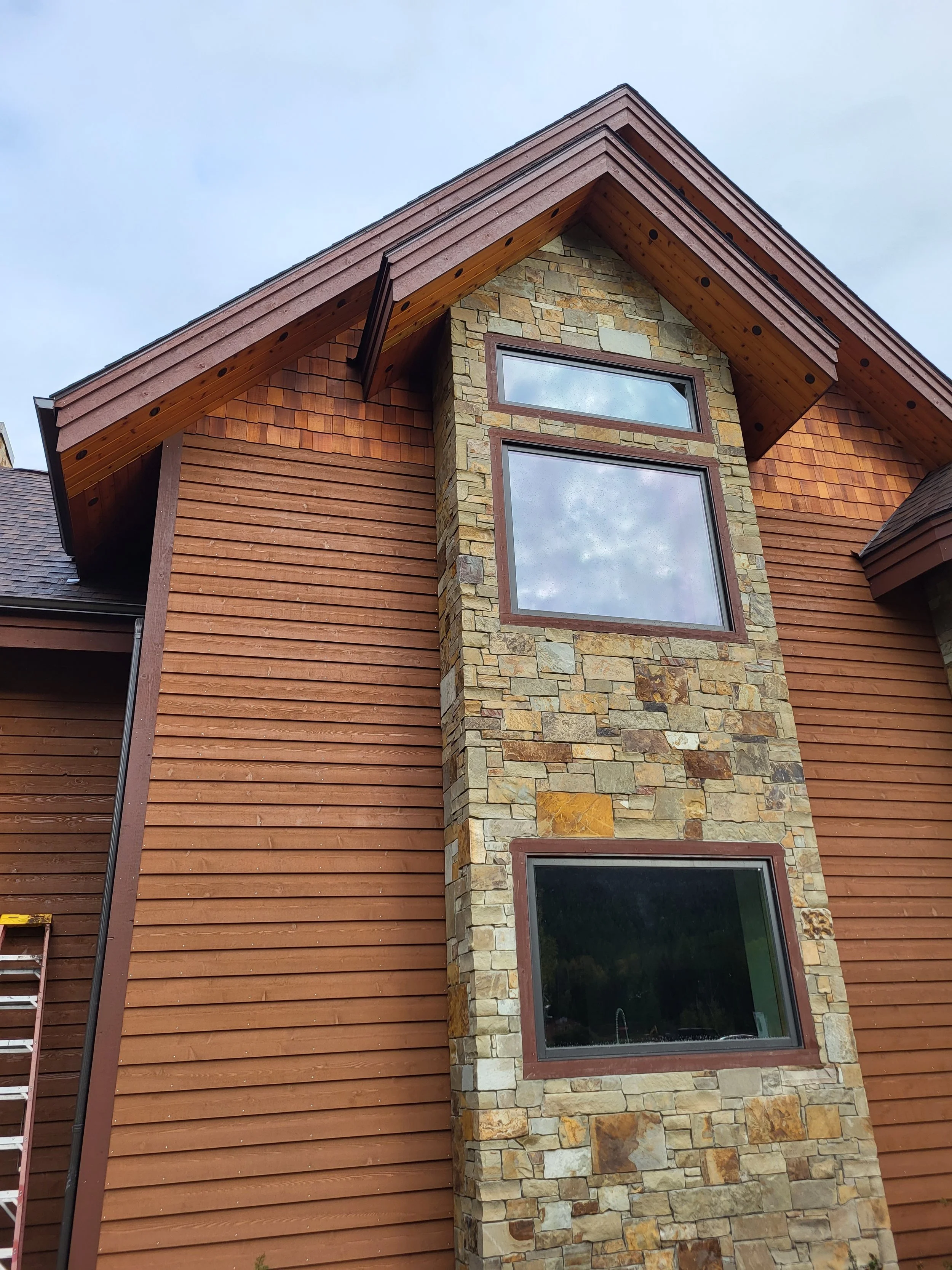 A close-up view of a house exterior featuring wood siding and a stone accent wall with three rectangular windows.