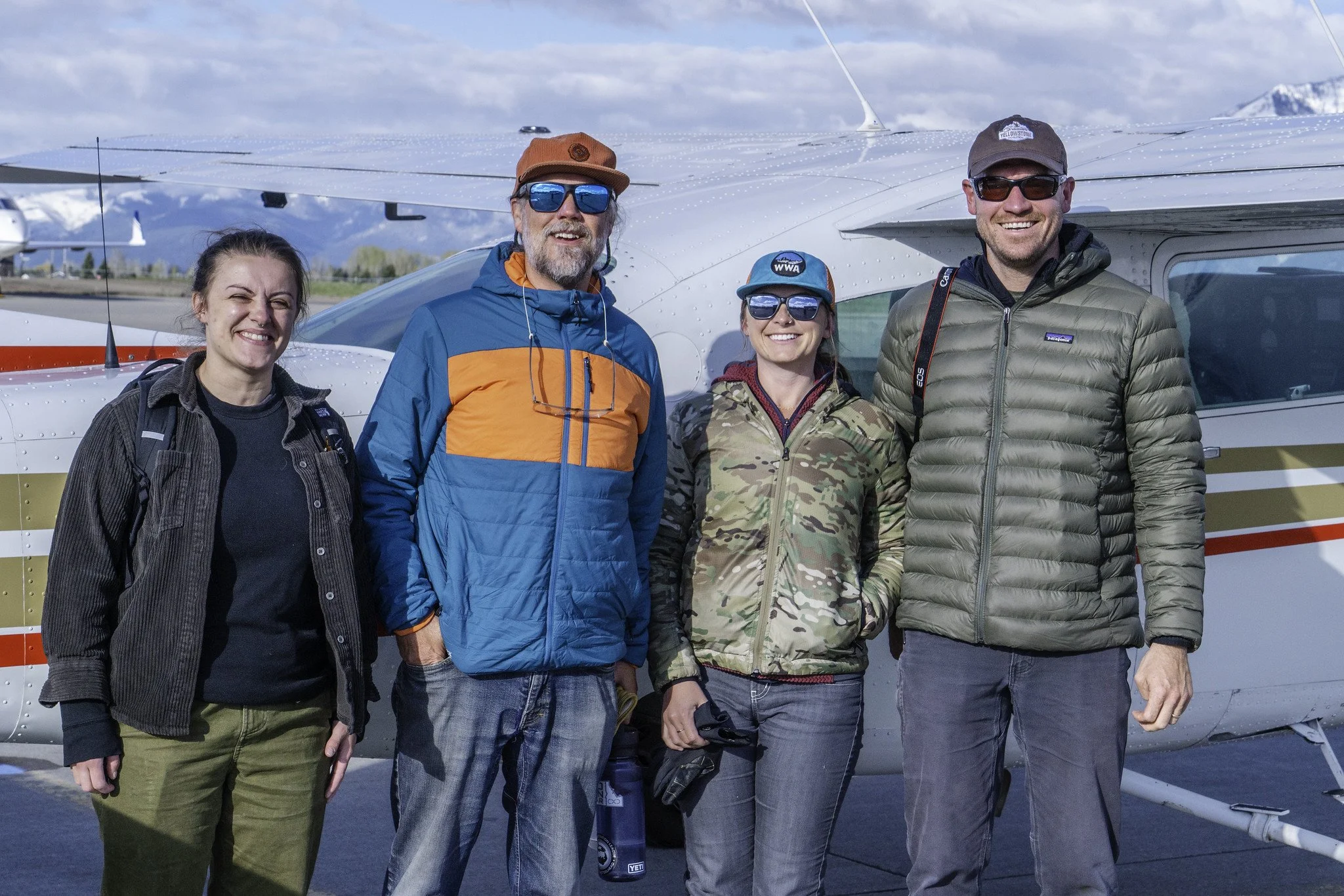 Four Bridger-Teton Together partners smile in front of a small plane.