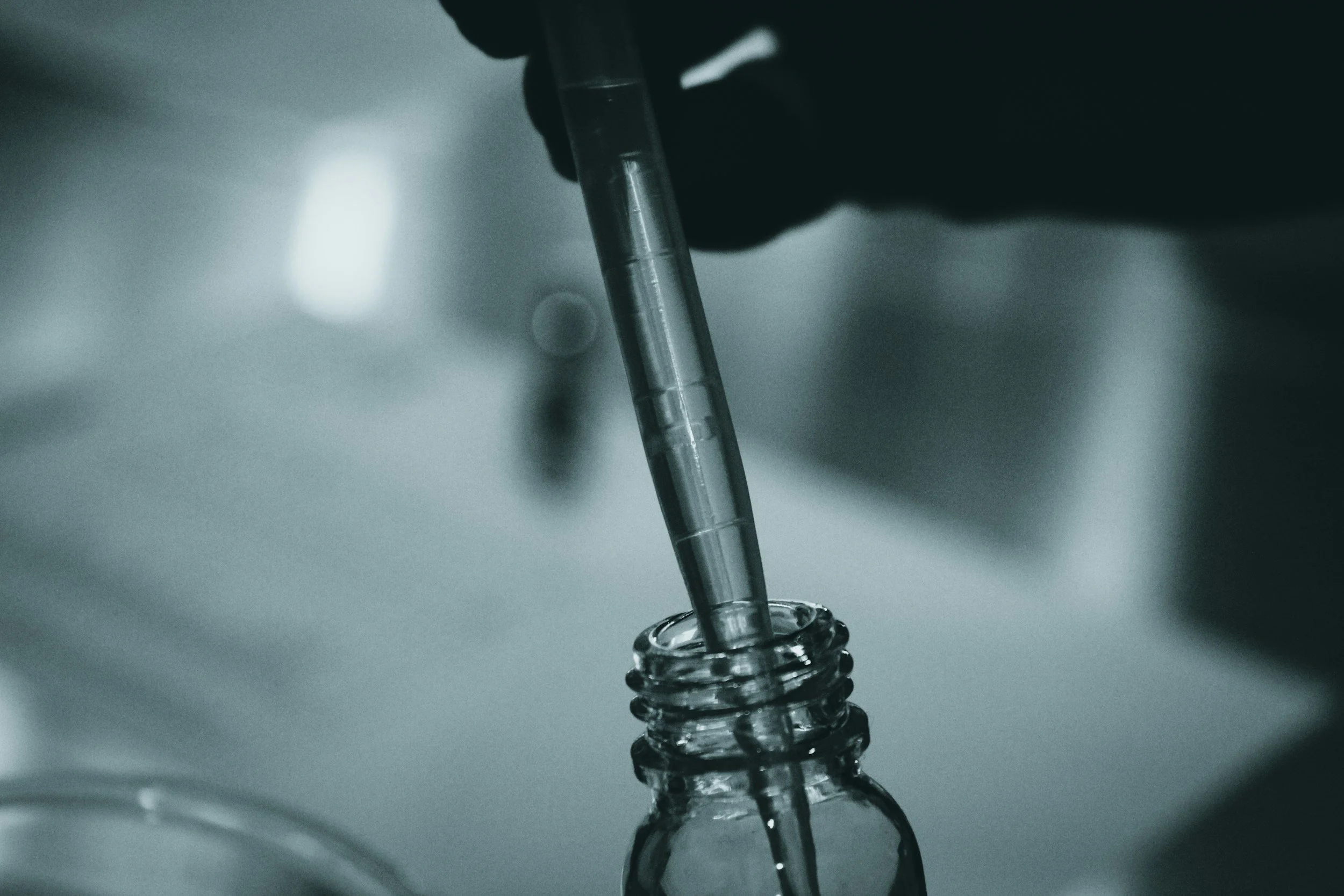 Close-up of a dropper inserting liquid into a small glass bottle, with a blurred background.