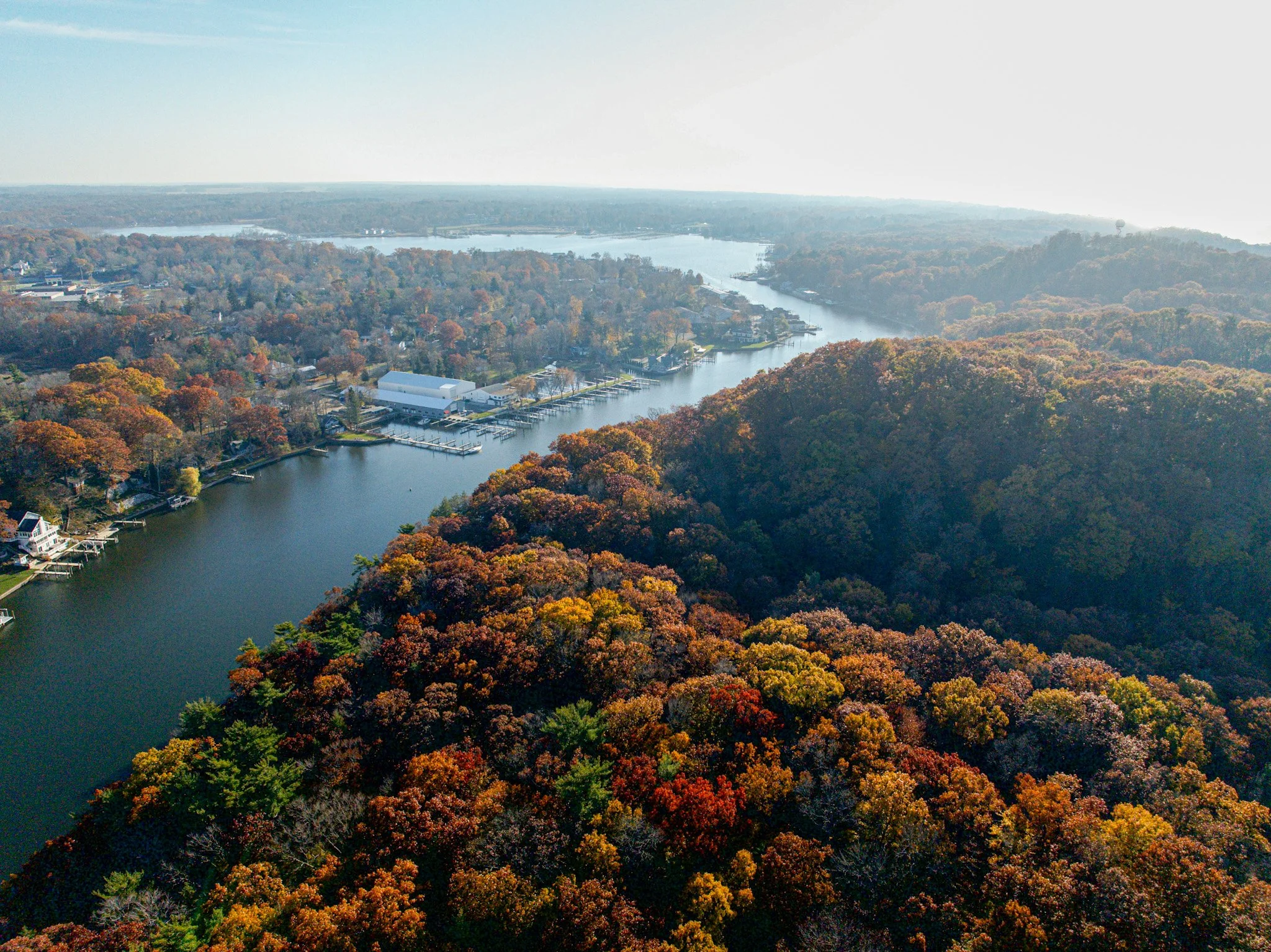 Aerial view of Kalamazoo river flowing through a forest with colorful fall foliage, residential homes, and a marina.