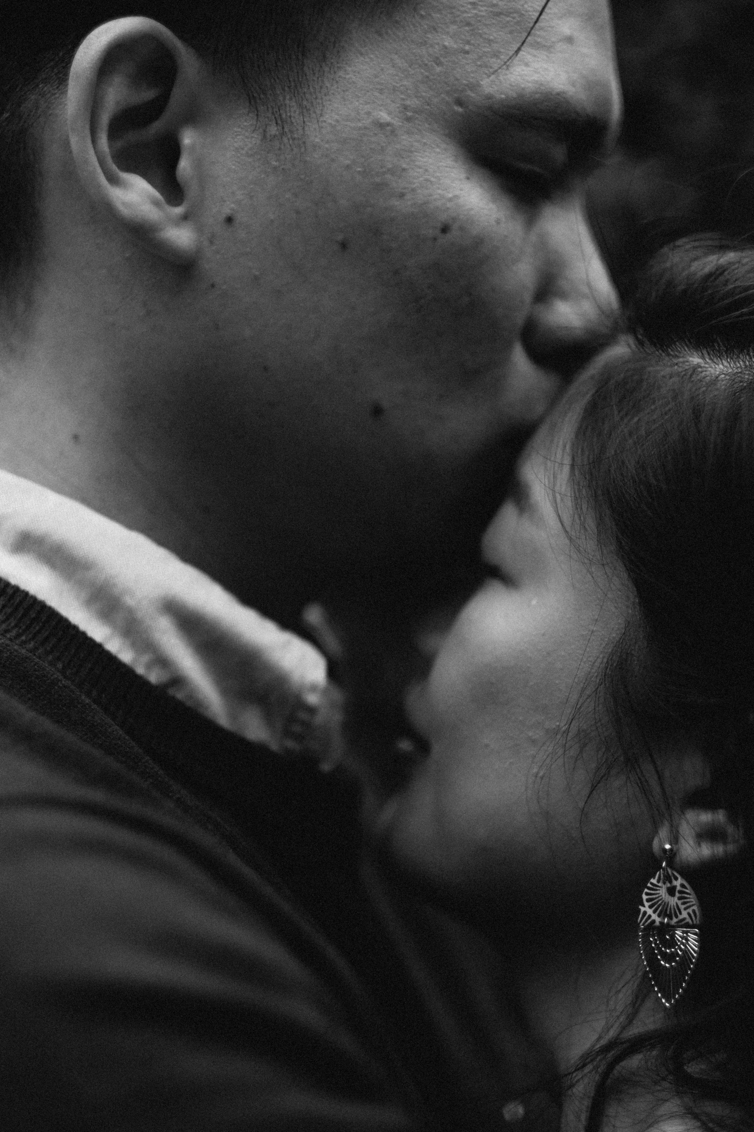 Un primer plano en blanco y negro de dos personas, una de ellas con oreja visible y la otra con mejilla y cabello visible, compartiendo un momento cercano y afectuoso, posiblemente un abrazo o beso