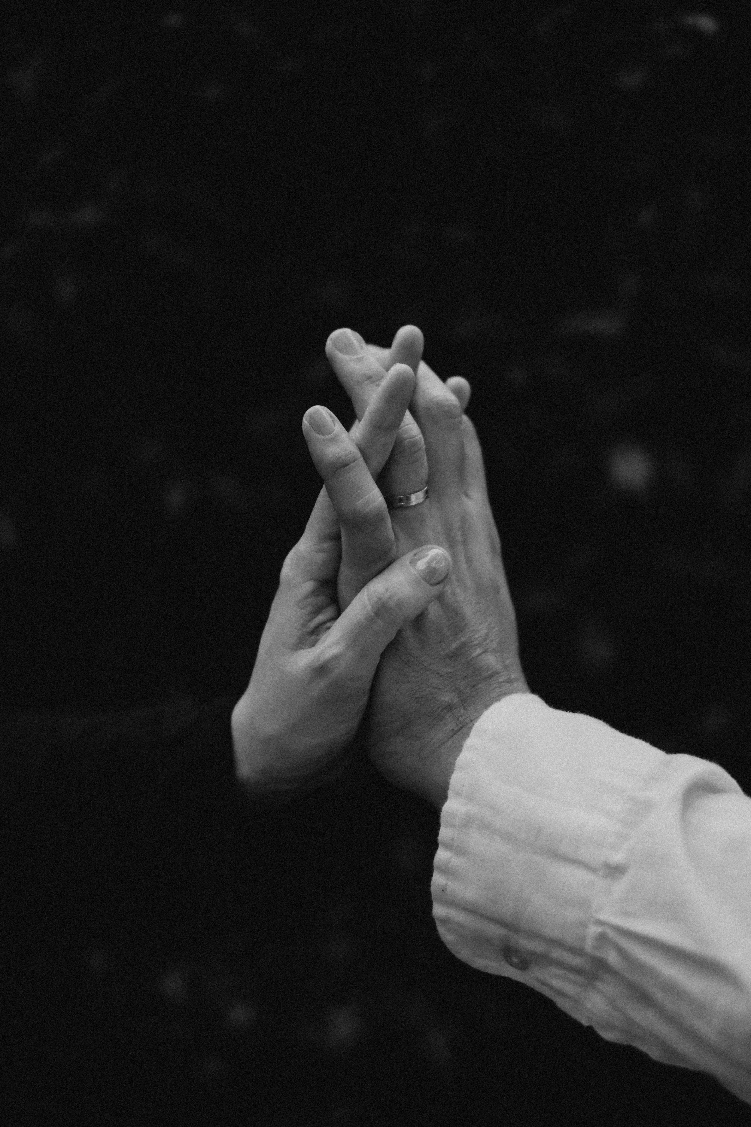 Dos manos entrelazadas en un fondo oscuro, una de ellas con una alianza, en un estilo en blanco y negro.