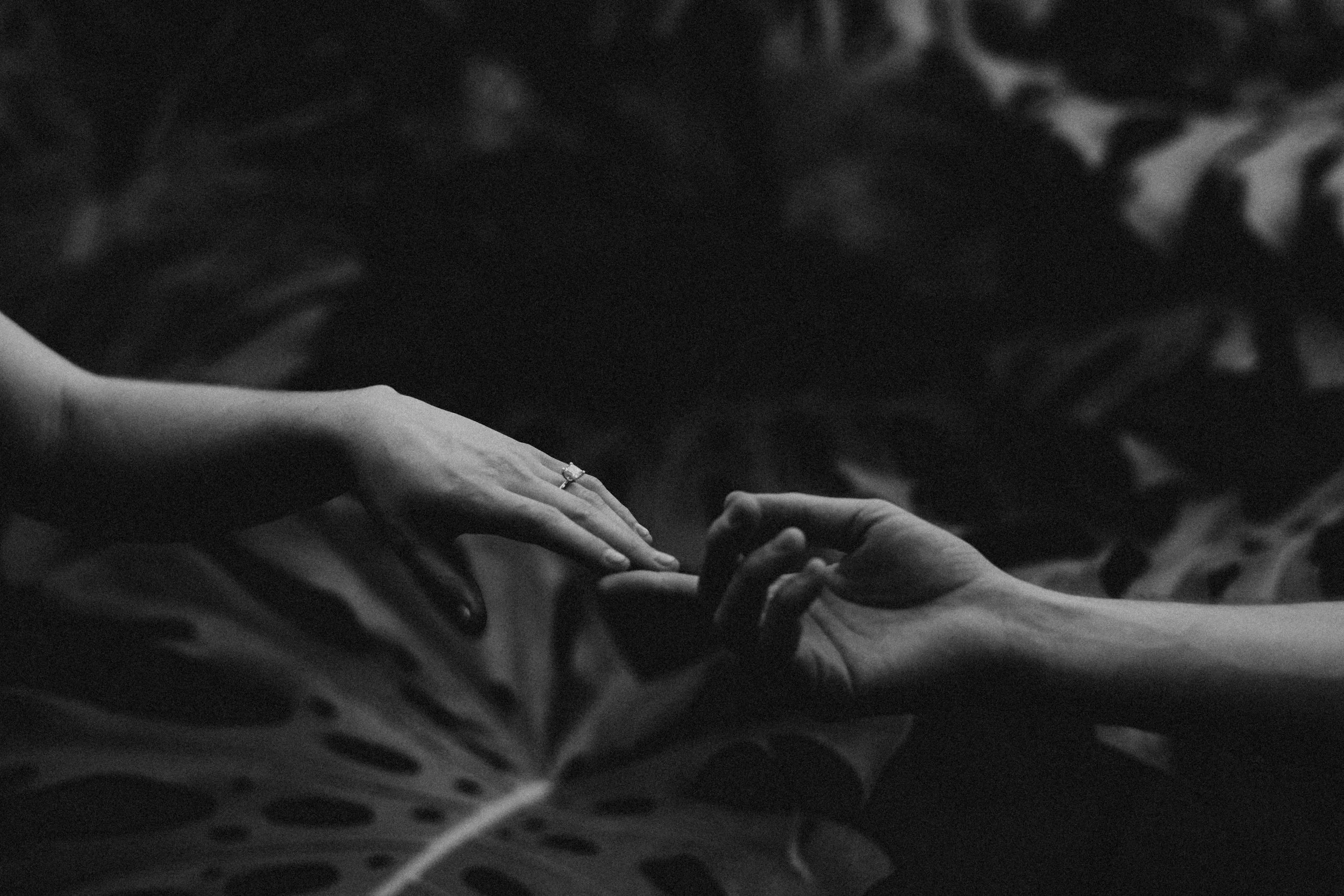 Dedos de dos personas tocándose, una con anillo, en un entorno oscuro.
