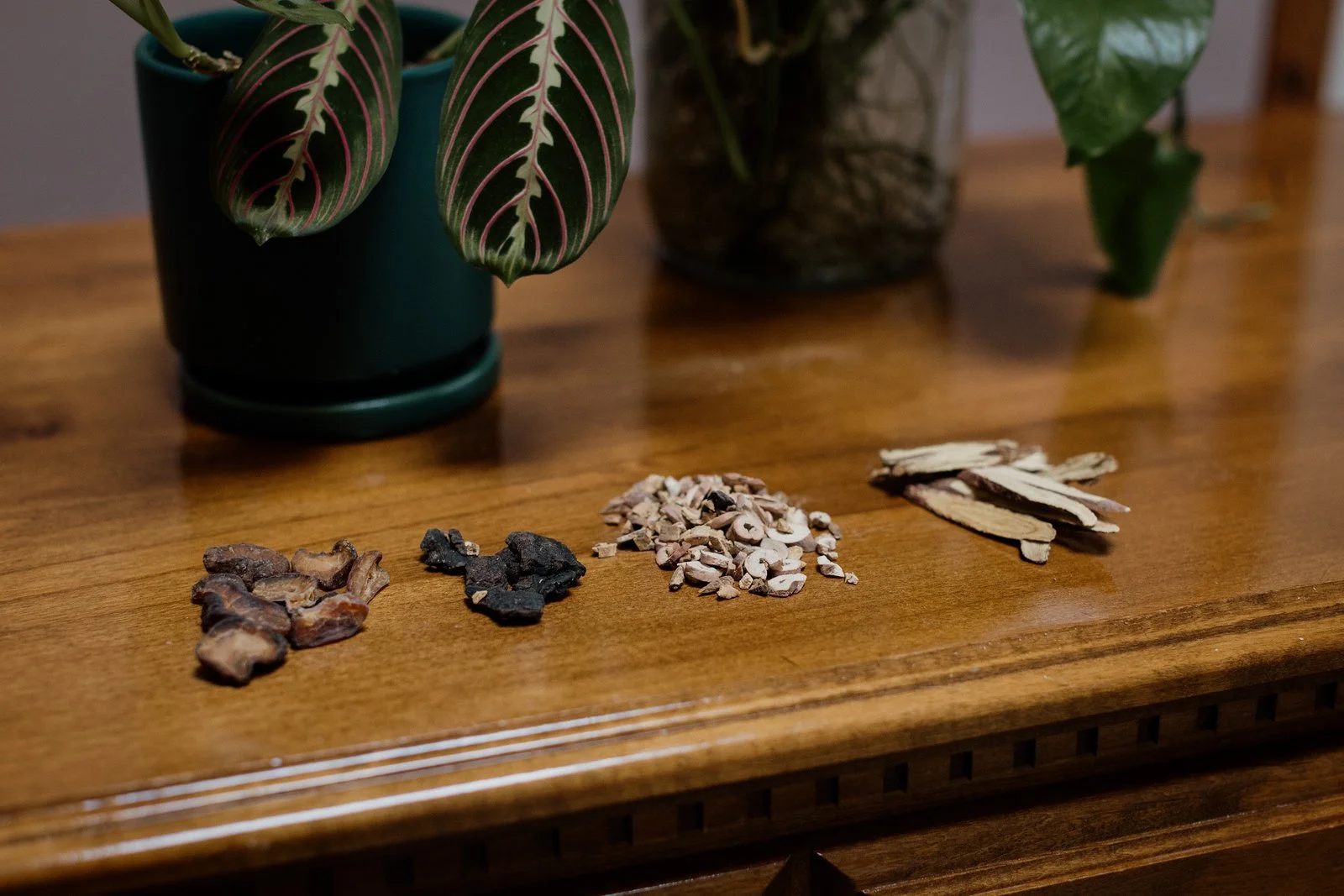 Four neat piles of medicinal herbs on a wooden surface and a plant in the background.