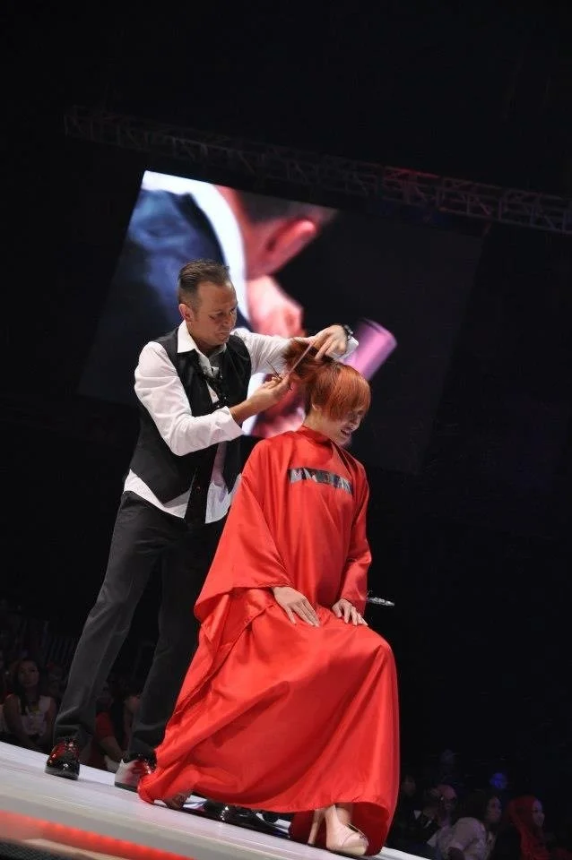 Darek on stage with a redhead woman and he is cutting her hair