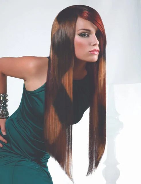 A woman with long, straight, brown hair with reddish highlights, wearing a teal dress, posing with her hand on her hip against a plain light background.