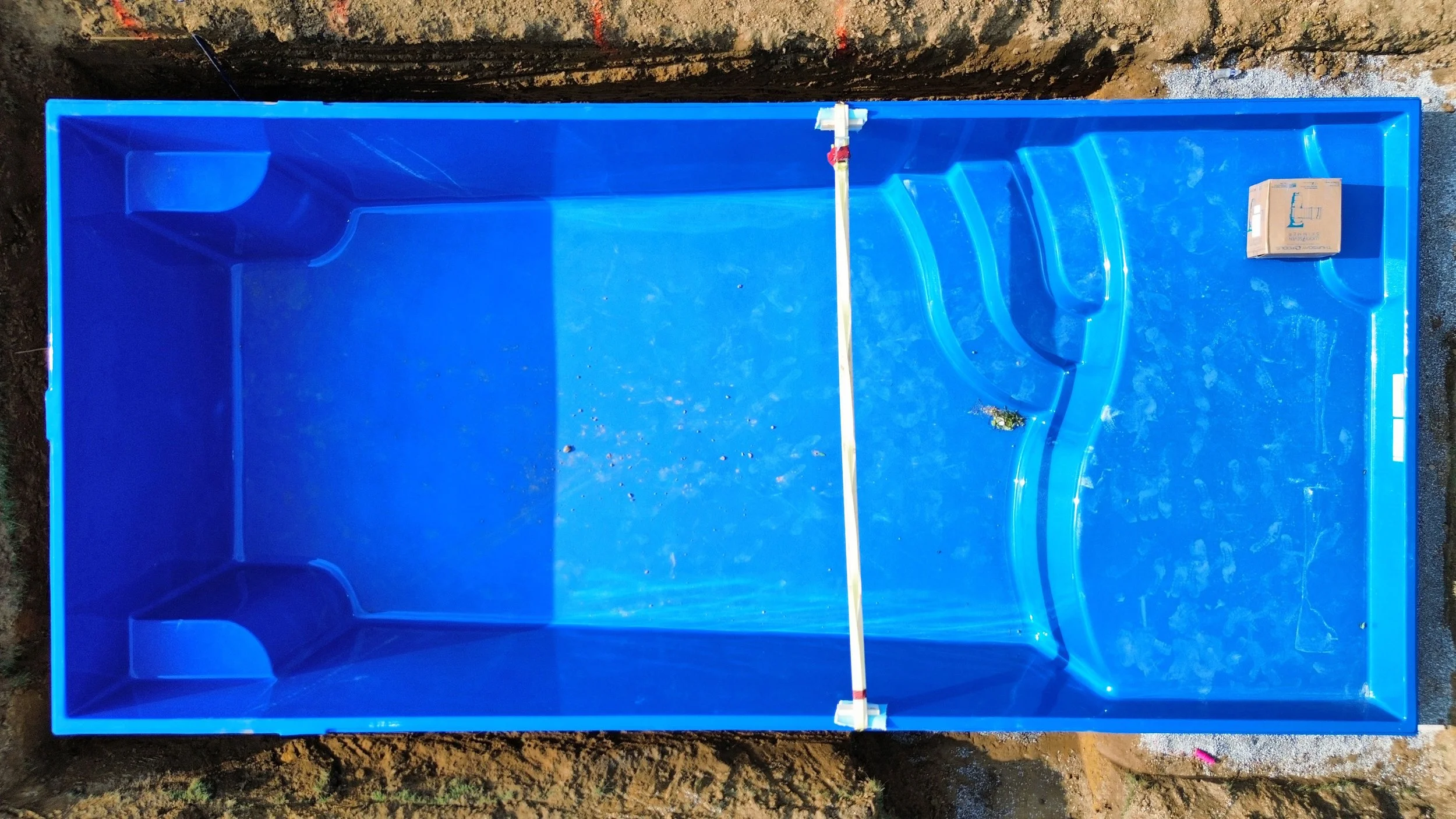 High-quality blue fiberglass pool shell with integrated steps and seating ledges during the leveling and plumbing phase of a residential installation.
