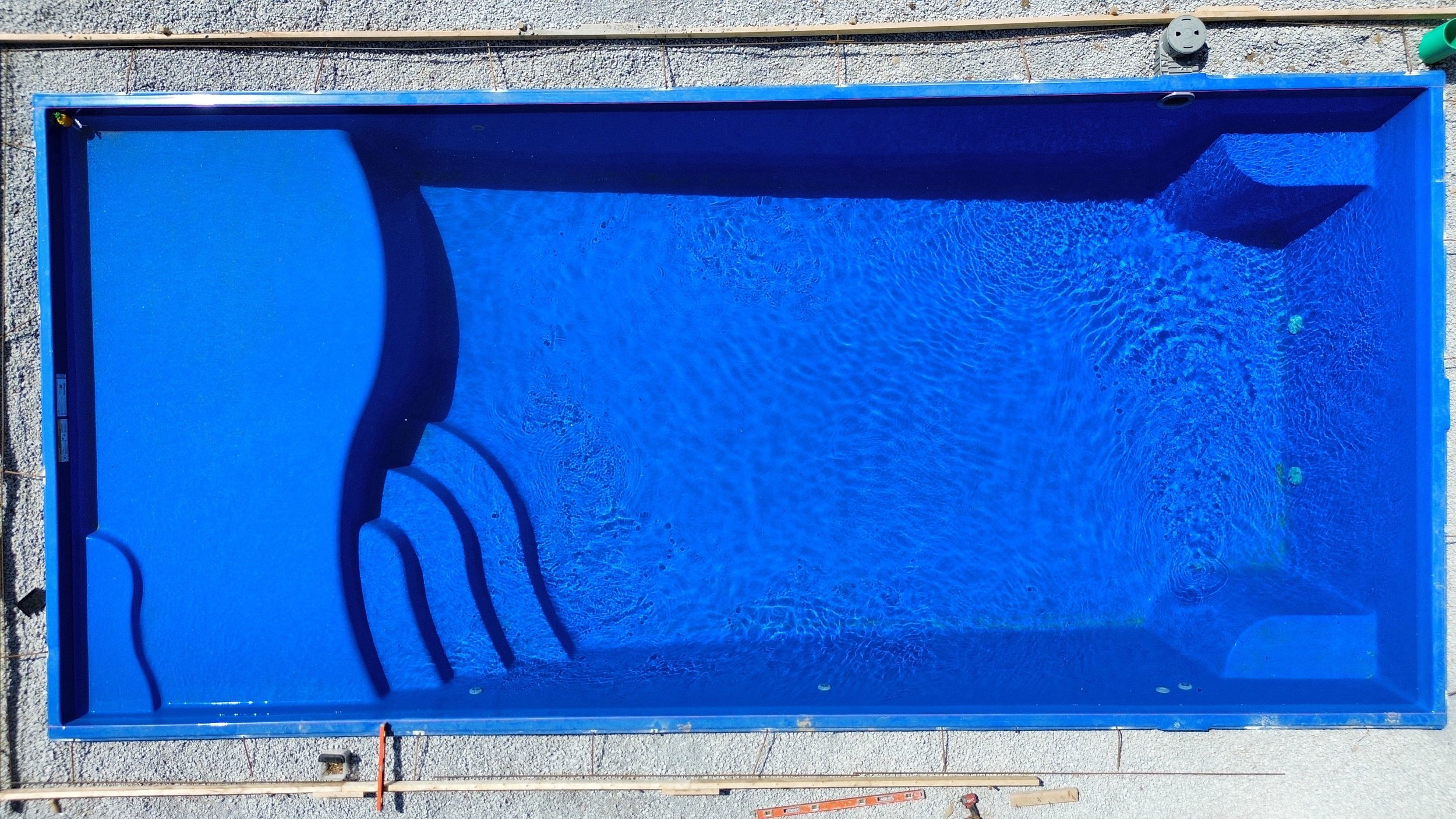 Blue rectangular swimming pool with stairs leading into it, viewed from above.