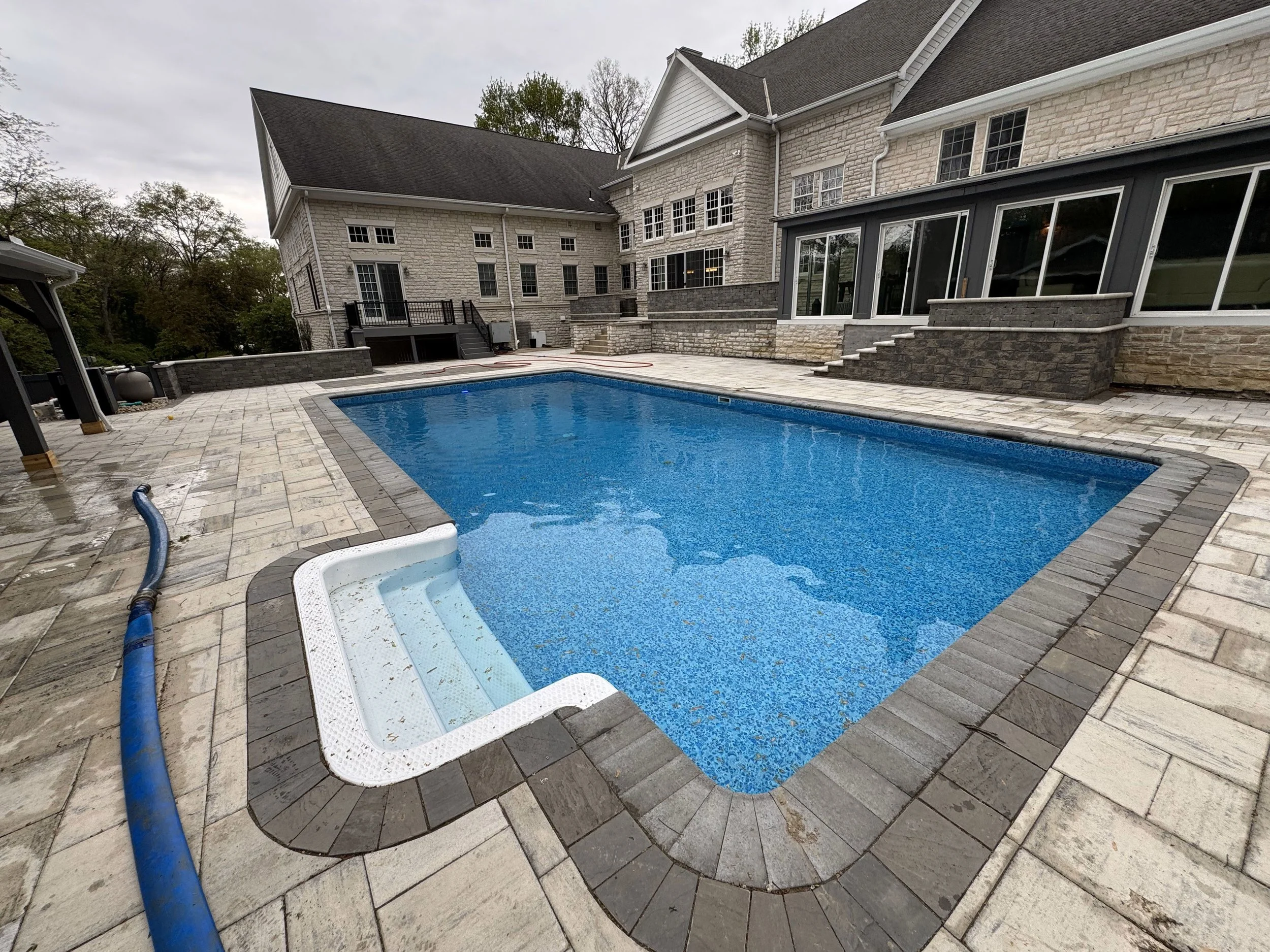 Replacement of a vinyl in-ground pool liner featuring a precision-fit design, integrated stairs, and matching dark grey stone coping for a luxury backyard renovation.