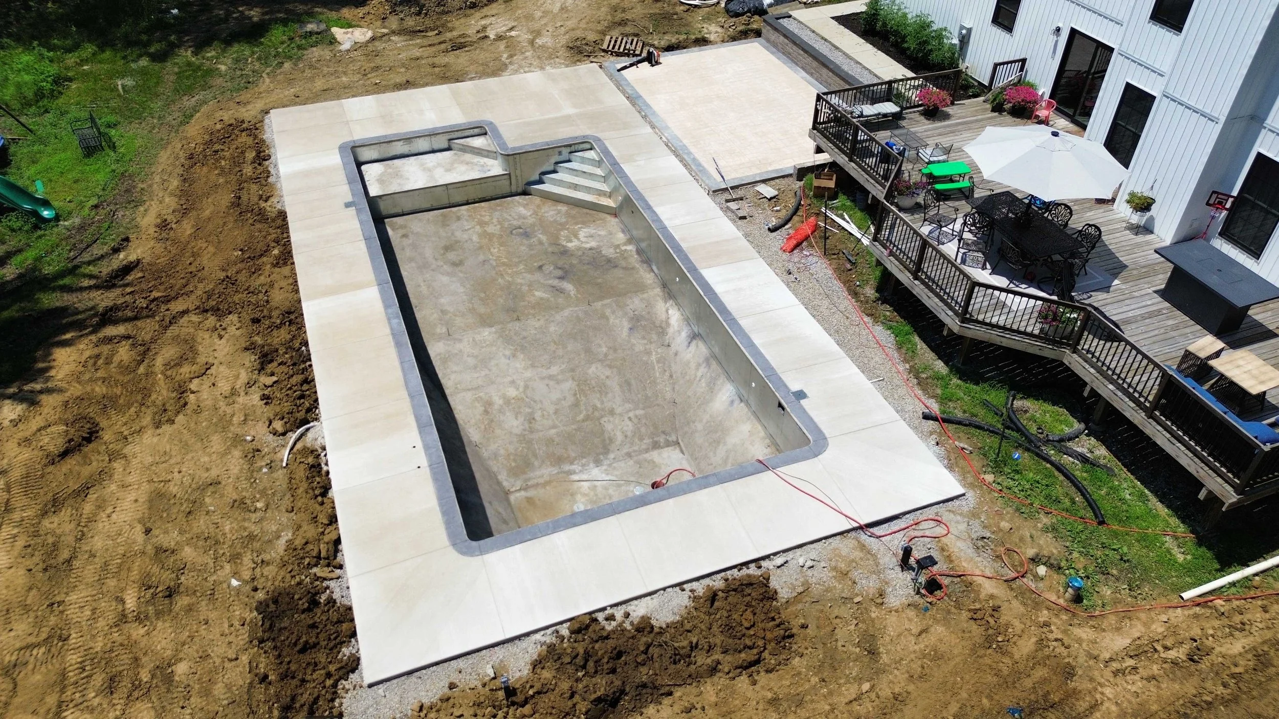 Aerial view of a custom residential in-ground pool under construction, featuring a precision-poured concrete deck and a deep-end excavation ready for liner installation.