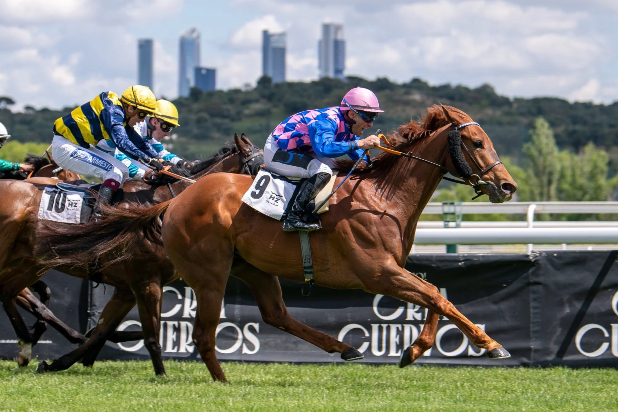 Jinete en un caballo de carreras en la pista, con otros jinetes detrás, durante una competencia.