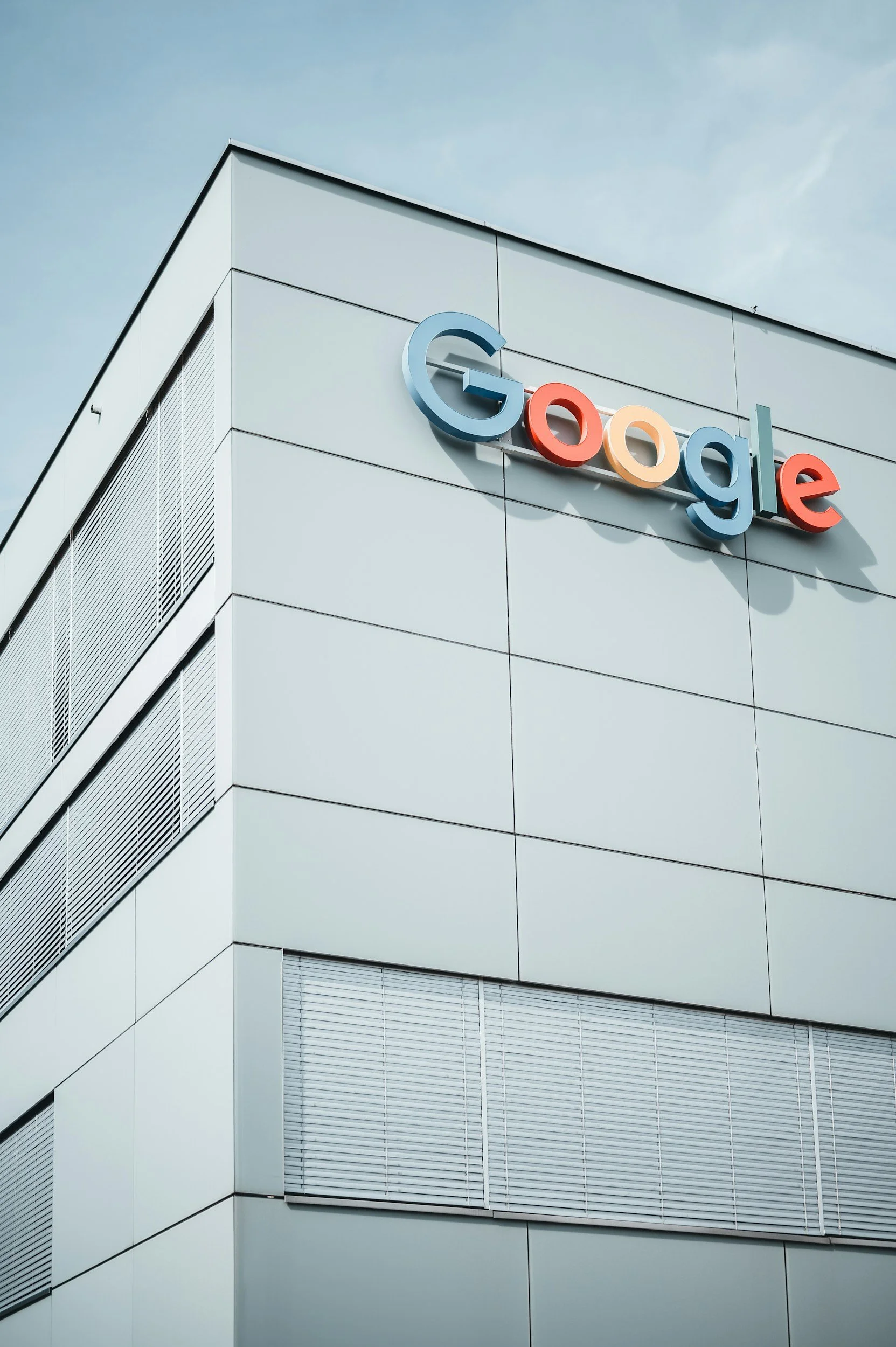 Modern building with an exterior sign that reads Google, with the letters in colorful 3D design, against a cloudy sky.