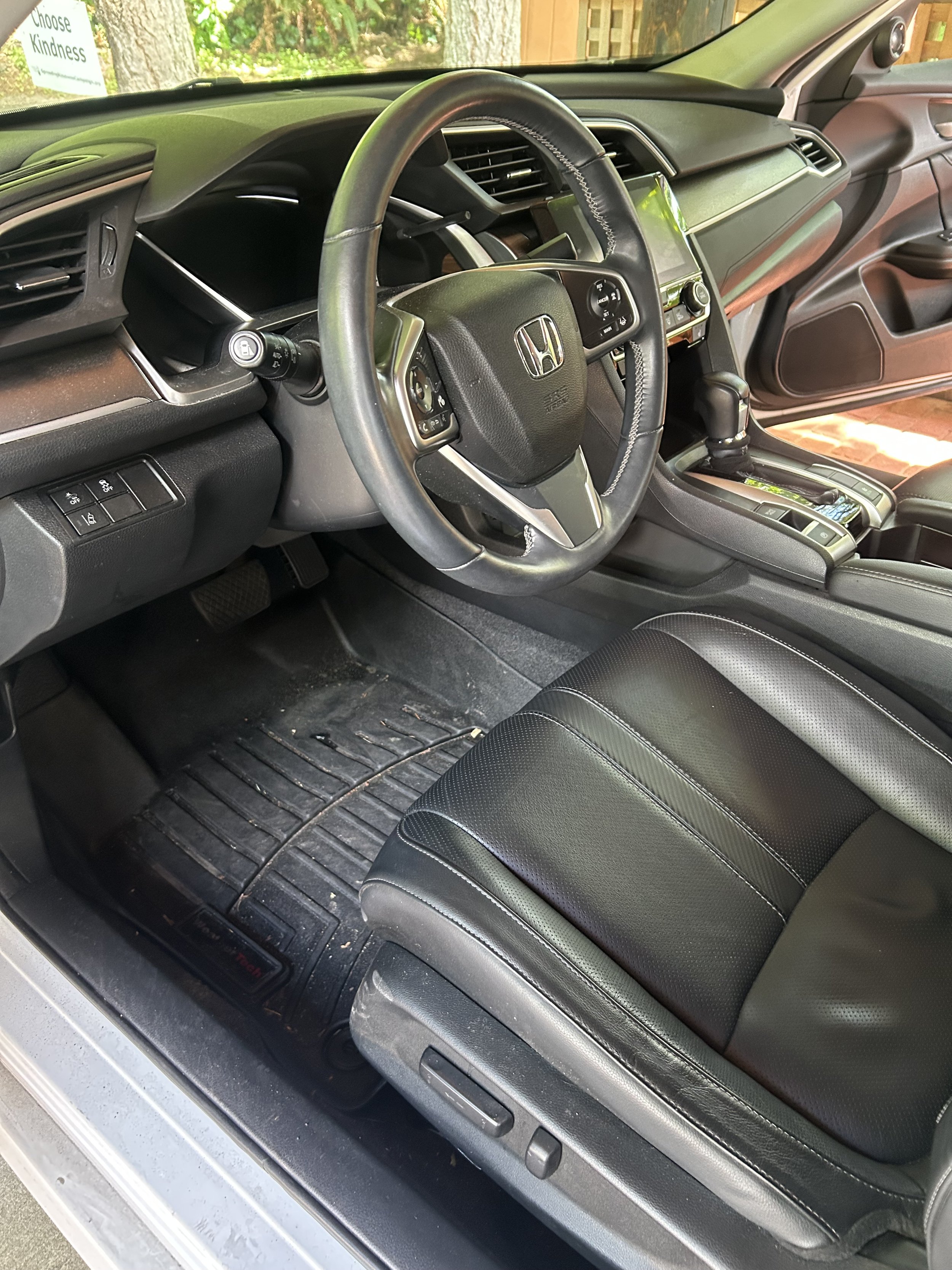 Inside view of a Honda vehicle's driver side showing the steering wheel, dashboard, instrument panel, gear shifter, and a part of the black leather seat.