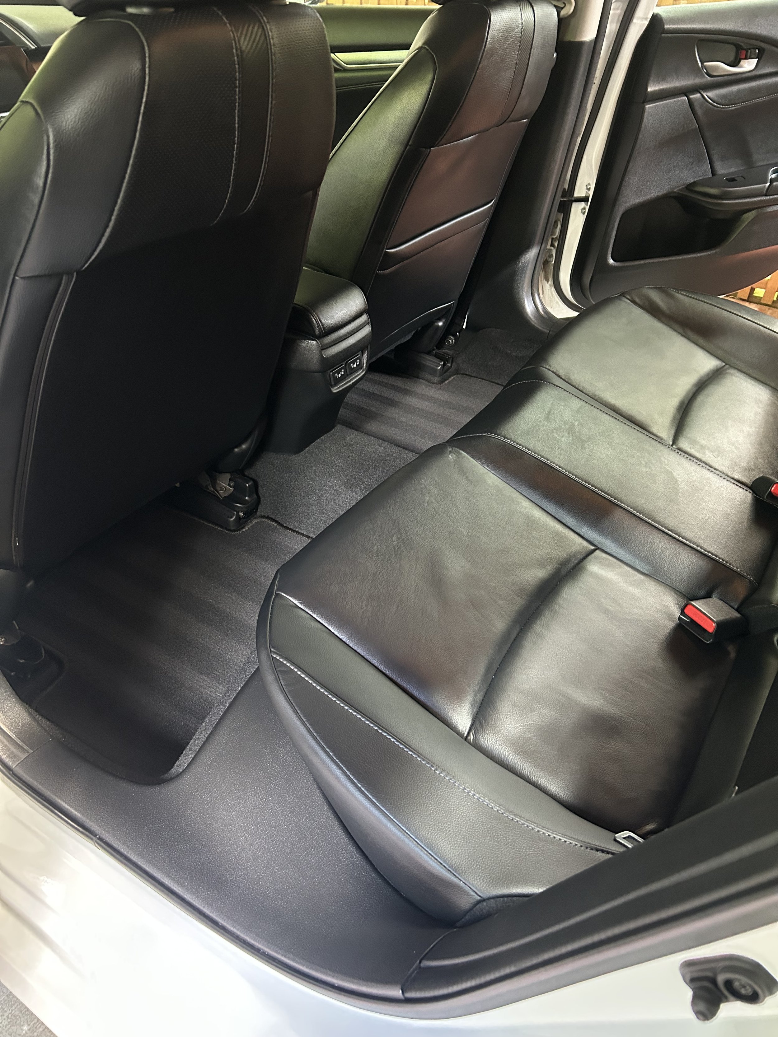 The backseat area of a vehicle showing black leather seats, a floor mat, and the bottom of the front seats.