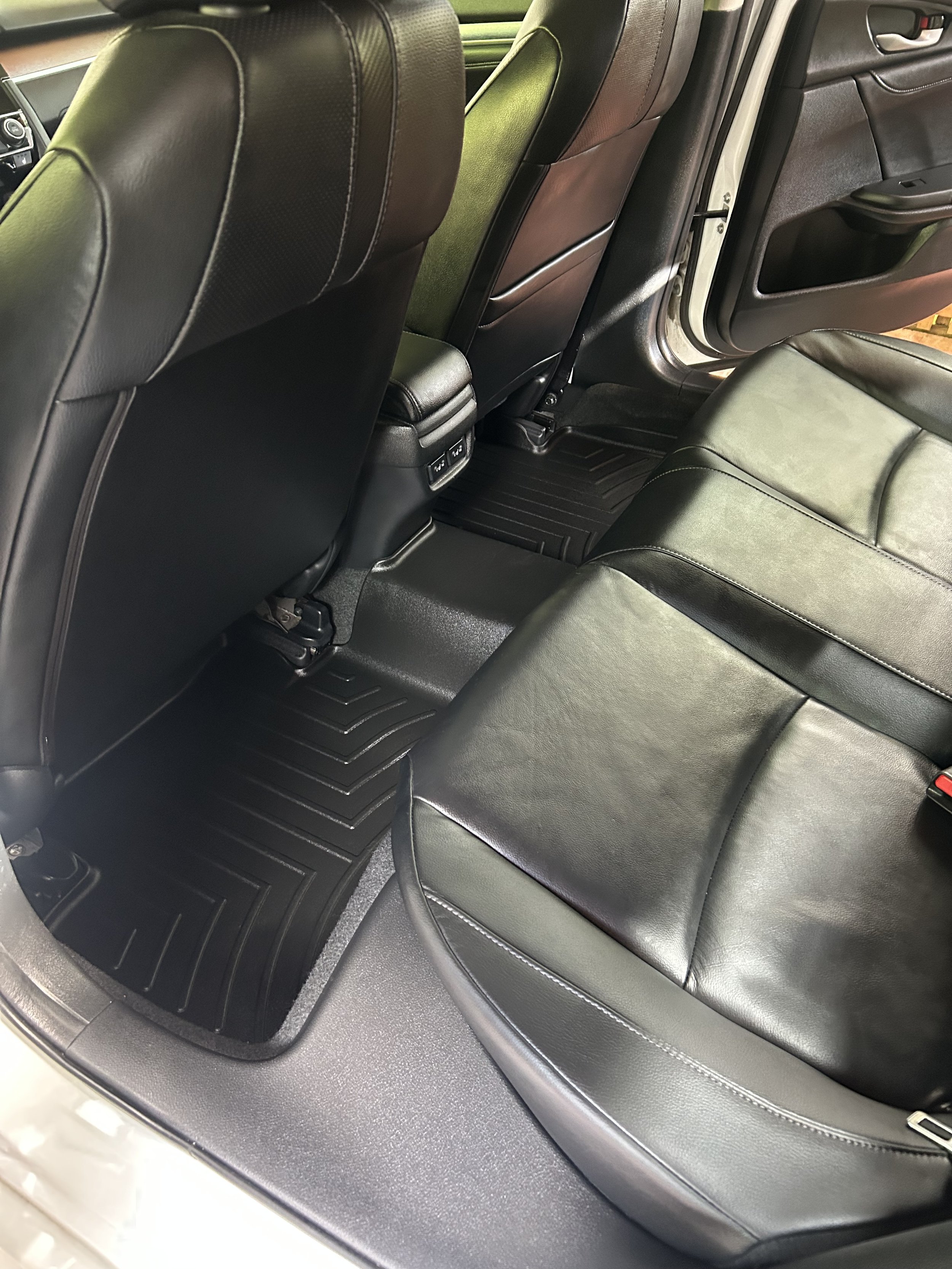 The back seat area of a car showing black leather seats, floor mats, and the back of the front seats.