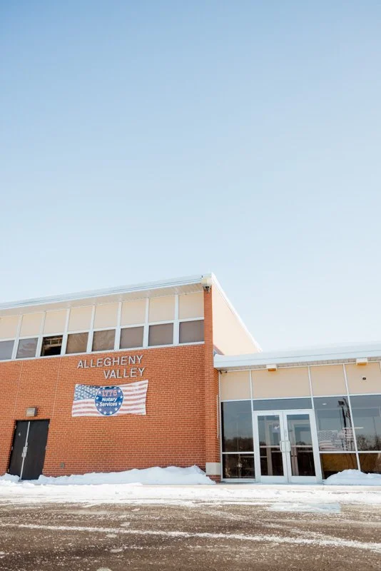 Allegany Valley building with a flag and snow on the ground under a clear blue sky.