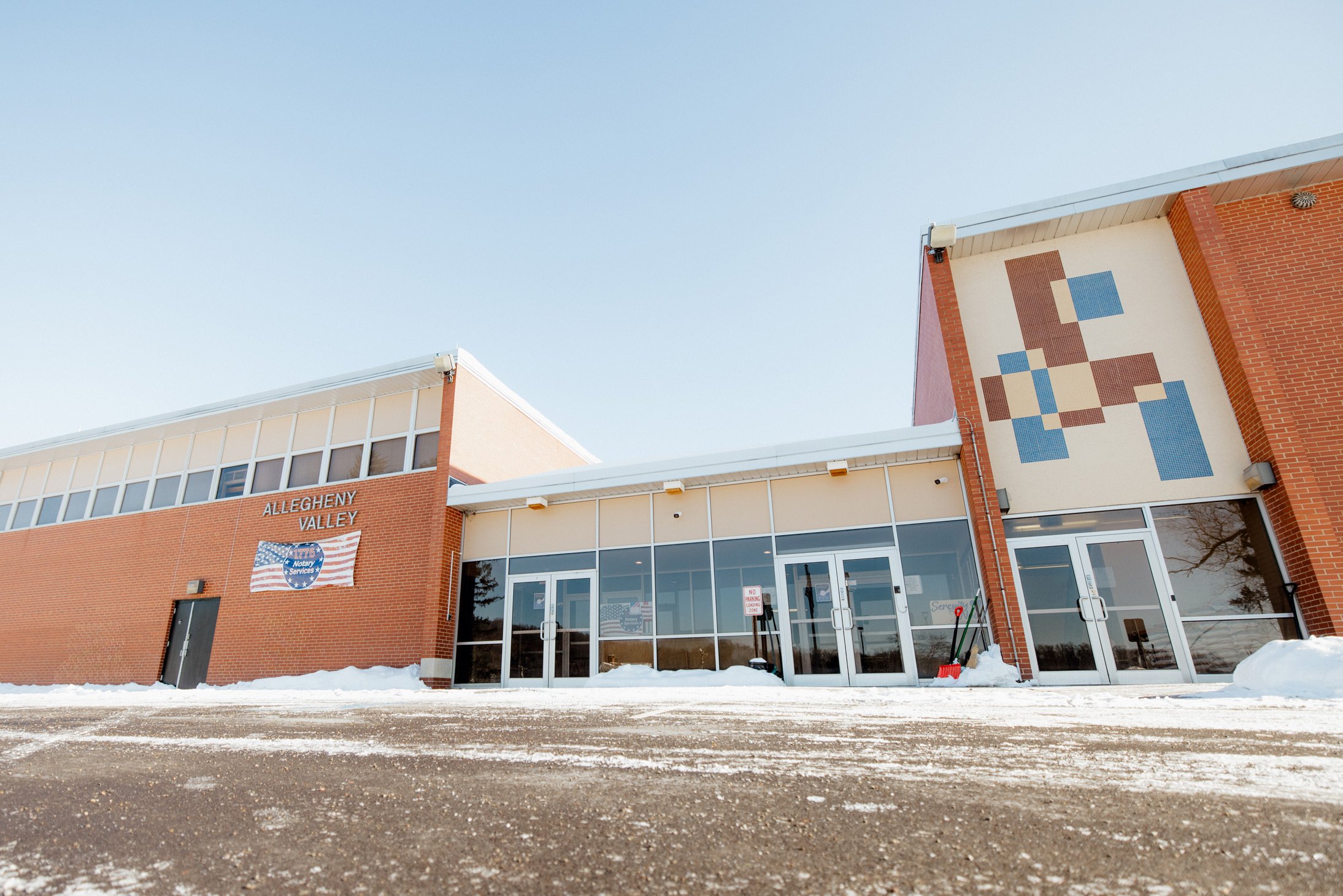 Exterior view of Allegheny Valley building with brick facade, large glass windows, and snow-covered ground.
