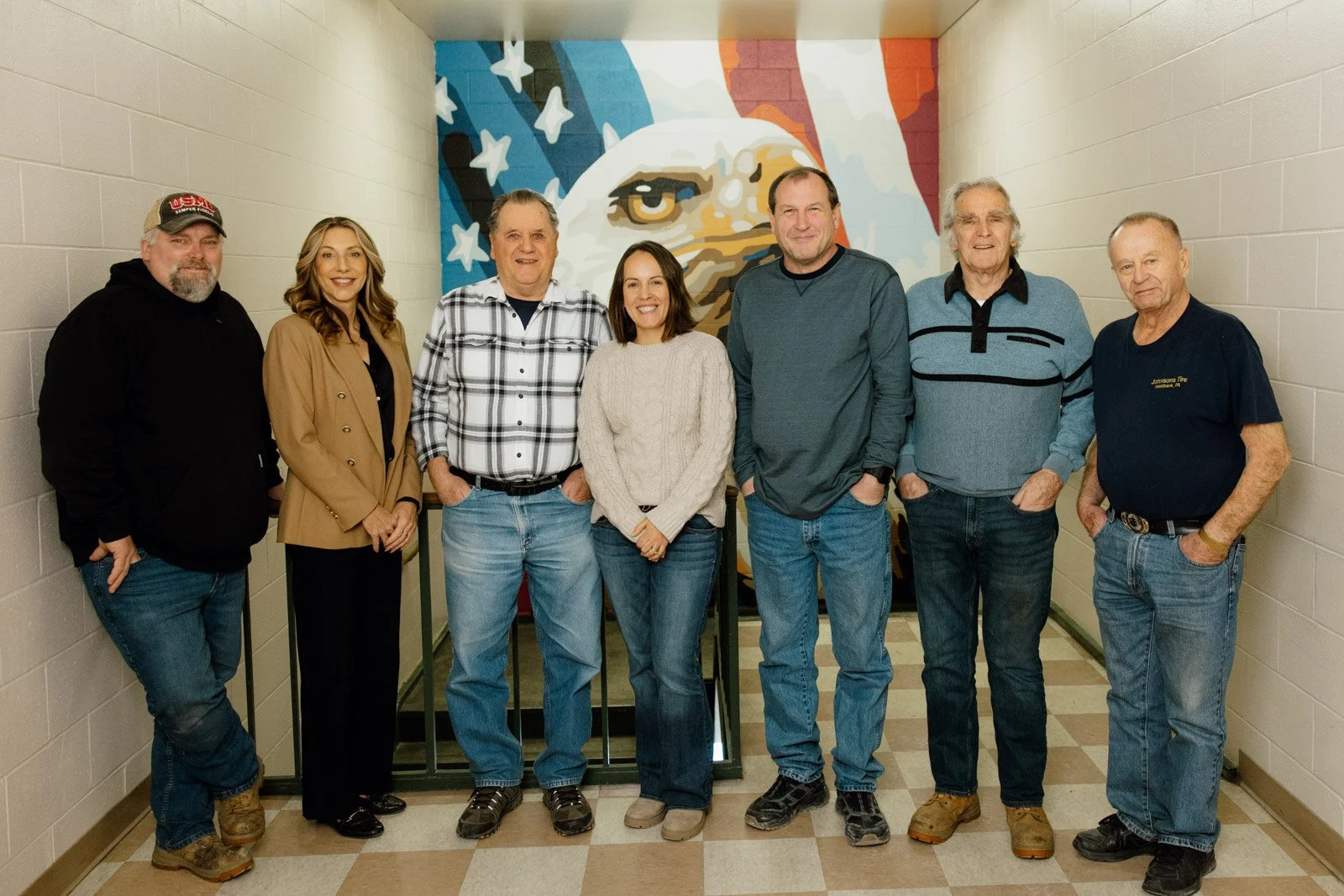Group of seven people standing inside a hallway in front of a mural of an eagle and American flag.