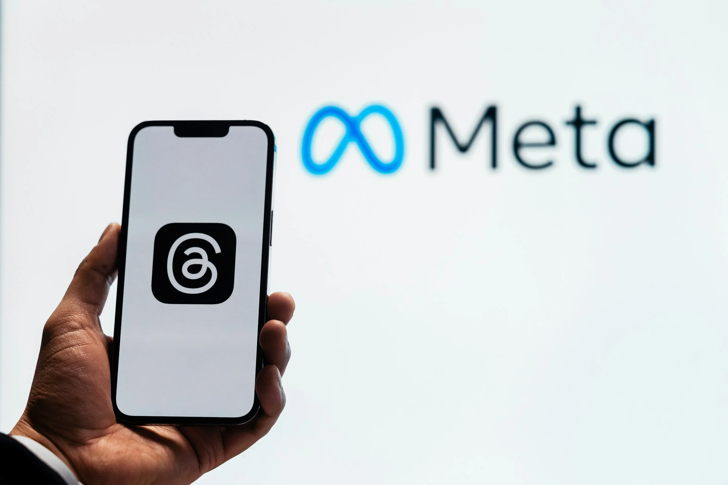 A person holding a smartphone with the Meta logo on the screen, in front of a blurred Meta logo sign.