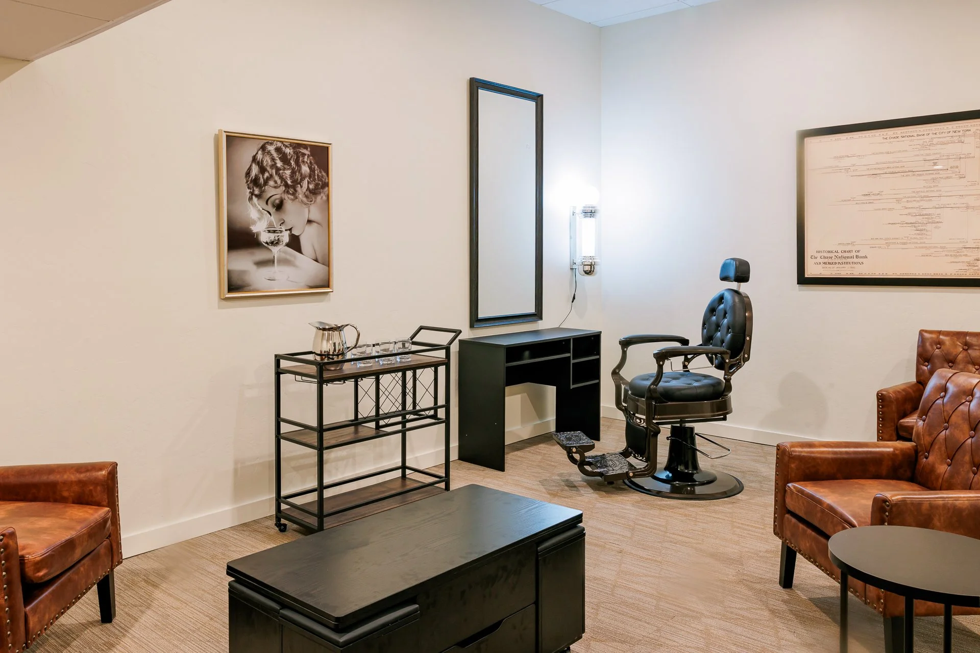 A vintage-style office or lounge with leather armchairs, a black desk, a barber or salon chair, and framed art on the walls, including a black and white photograph of a woman drinking from a glass.