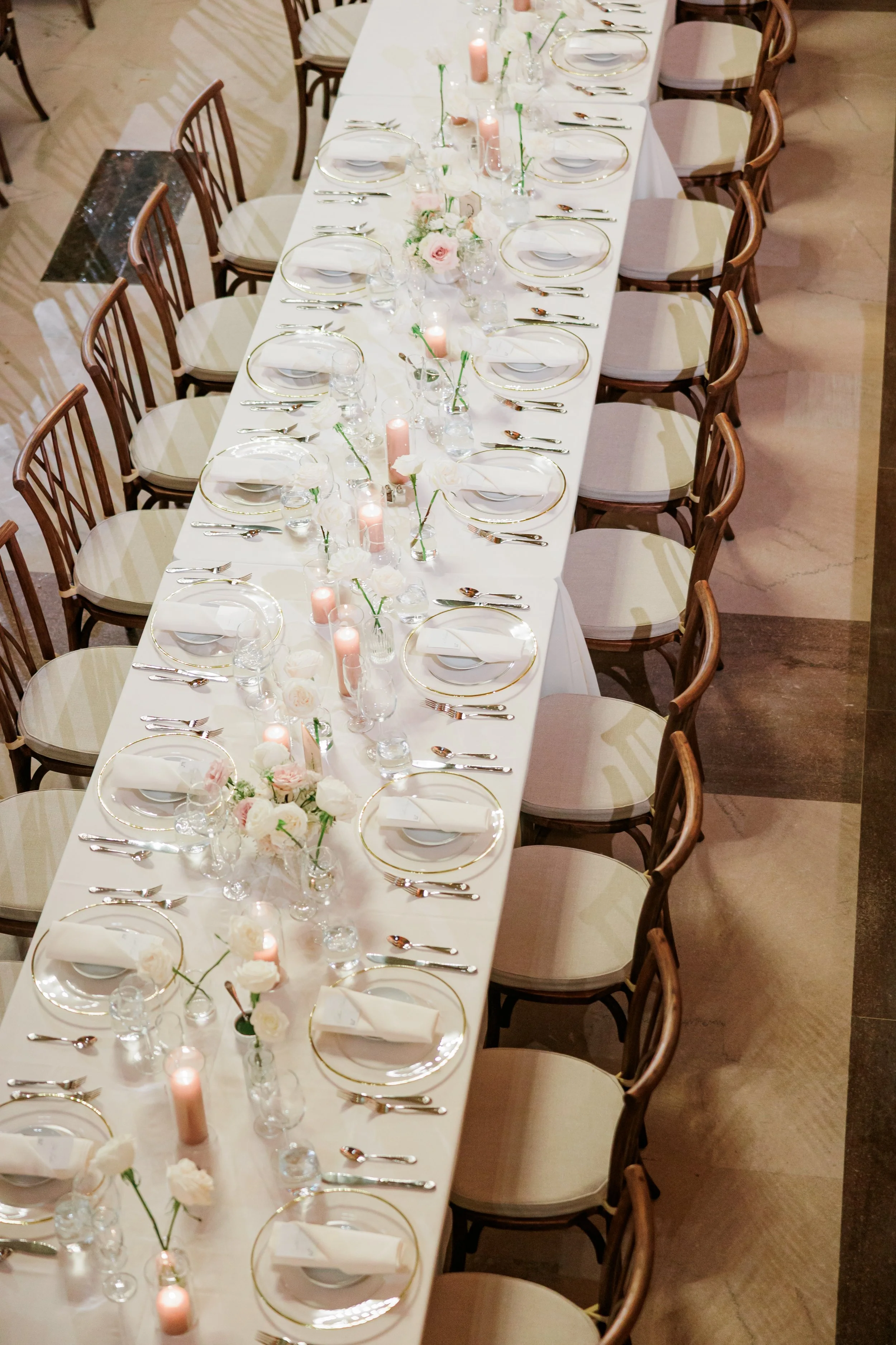 Elegant dining table set for a special occasion with floral centerpieces, candles, glassware, and gold-rimmed plates.