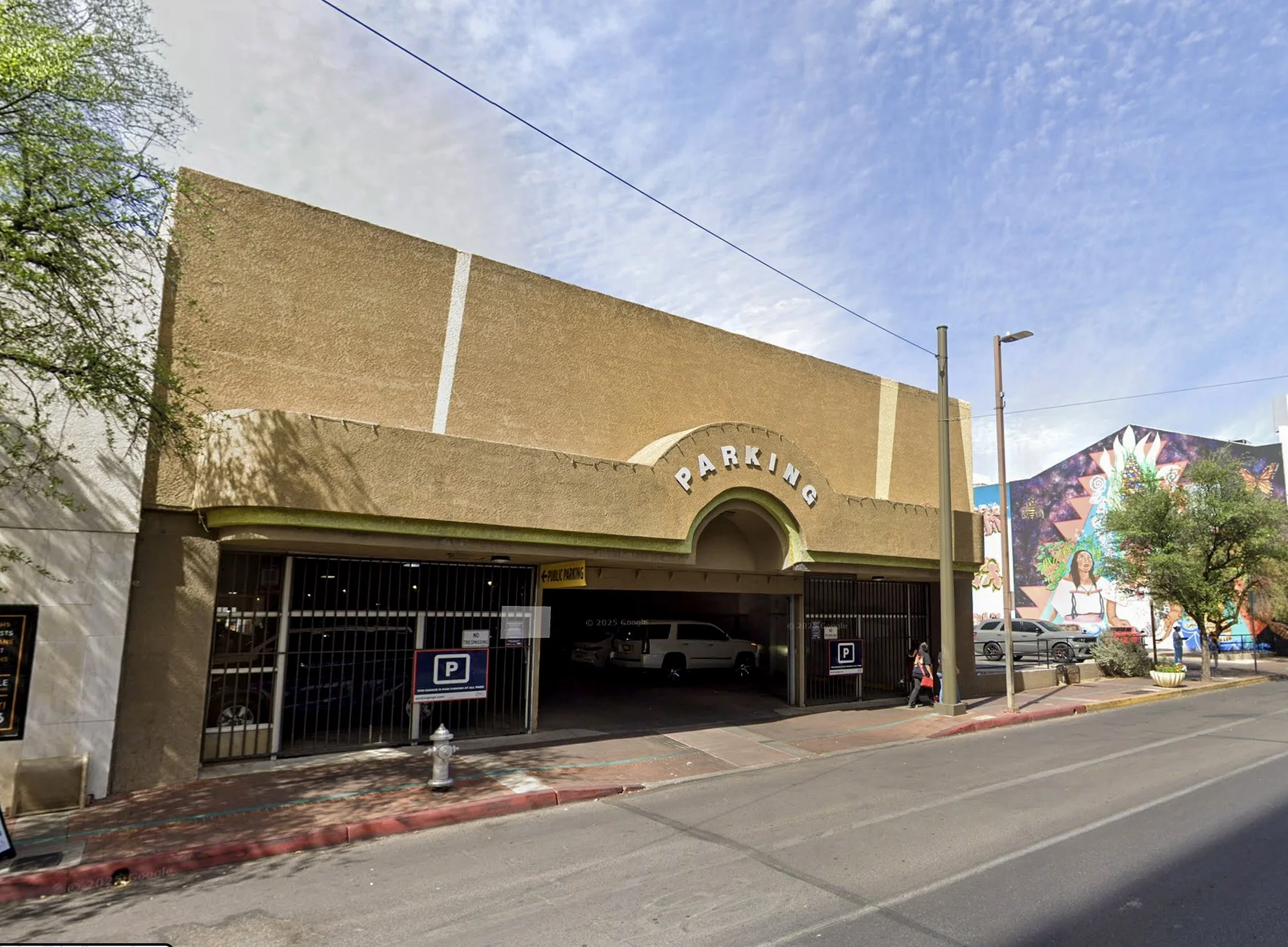 A parking garage with an arched entrance and the word 'PARKING' on top, next to a colorful mural of a woman surrounded by nature.