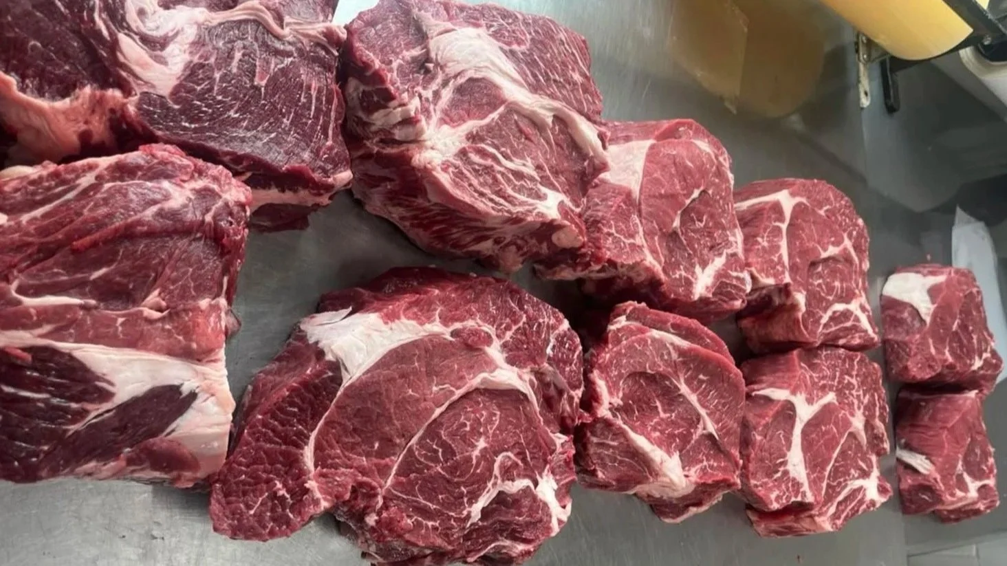 Several large cuts of raw beef steaks with marbling, placed on a metal surface.