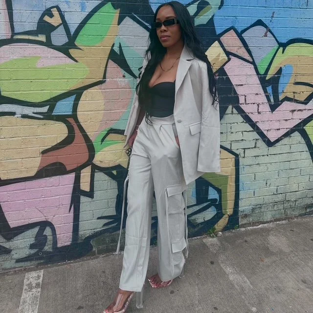 Woman in beige suit with black top and sunglasses standing in front of colorful graffiti wall.