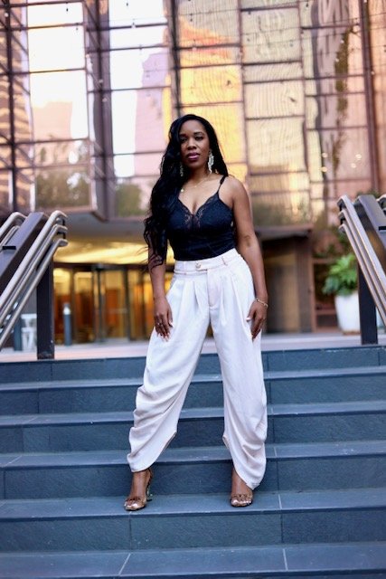 Woman standing on outdoor stairs in front of glass building, wearing black top and white pants.