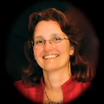 Portrait of a woman with glasses, curly brown hair, smiling, wearing a red top, against a dark background.