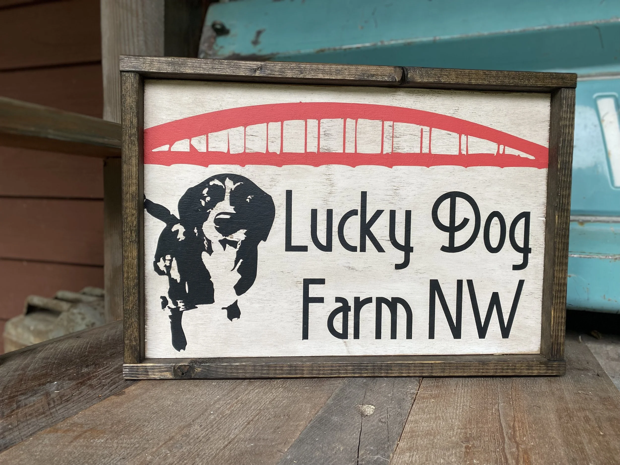 Sign that reads 'Lucky Dog Farm NW' with a silhouette of a dog and a red bridge illustration above the text.