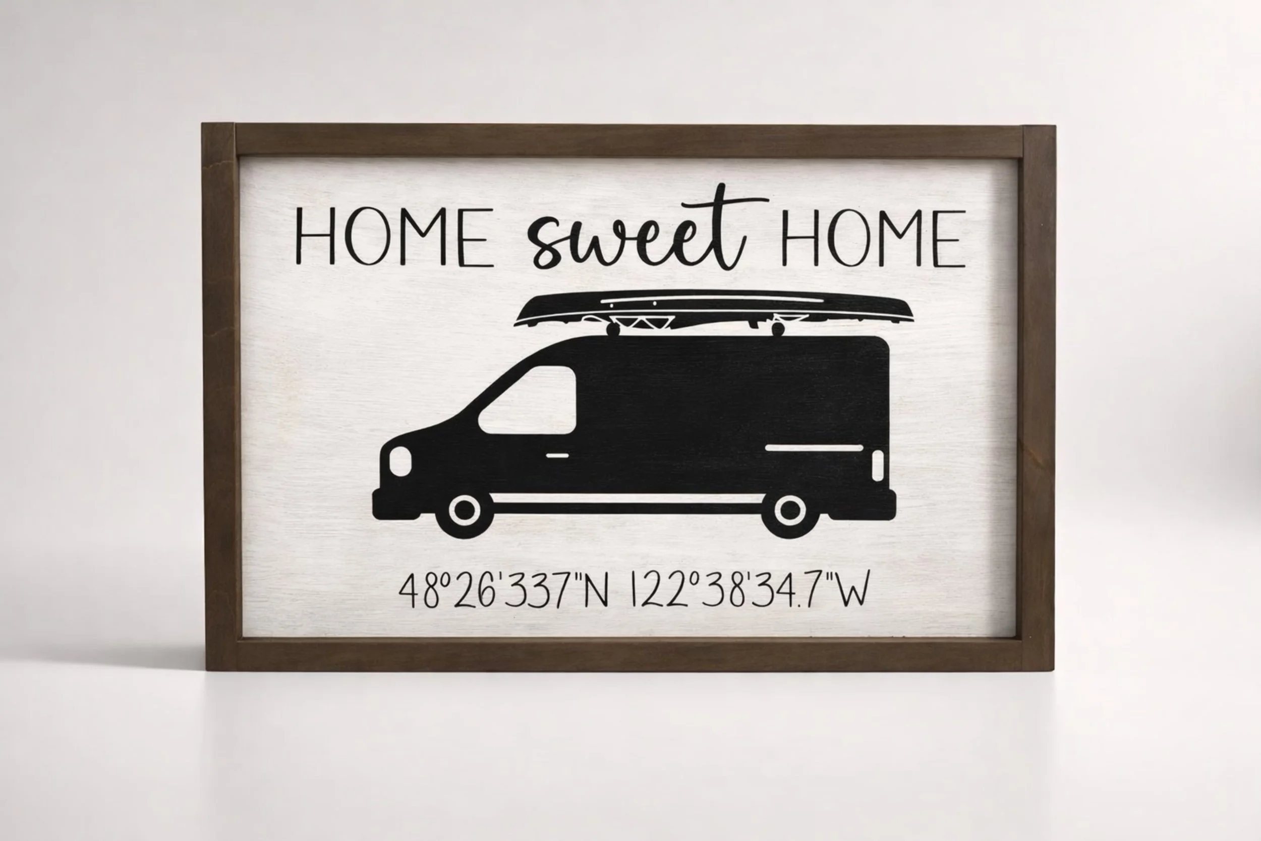 Decorative sign with the words 'Home sweet home', a silhouette of a van with a surfboard on top, and coordinates '48°26'33.7"N 122°38'34.7"W'.
