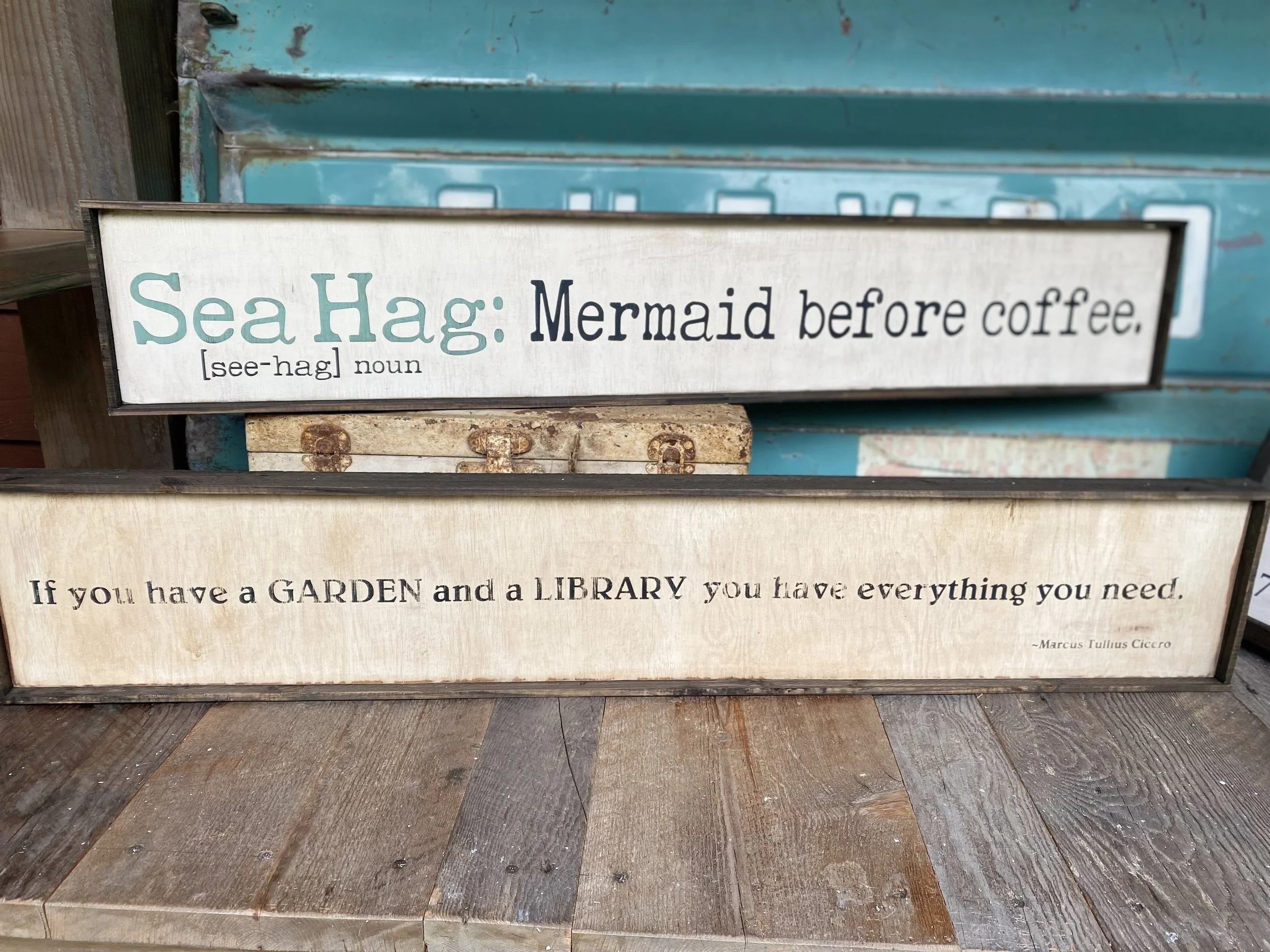 Decorative sign with the text "Sea Hag: Mermaid before coffee. [see-hag] noun" on a wooden surface.