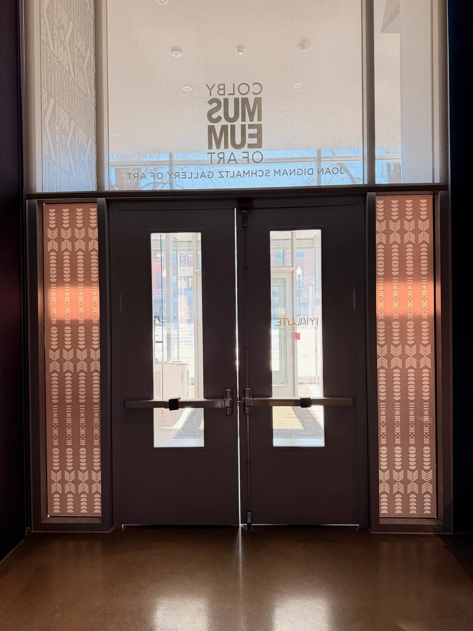 Double glass doors at the entrance of a museum, with decorative panels on each side and signage above reading 'Museum of Art' and 'Don Davis Schmalz Gallery of Art'.