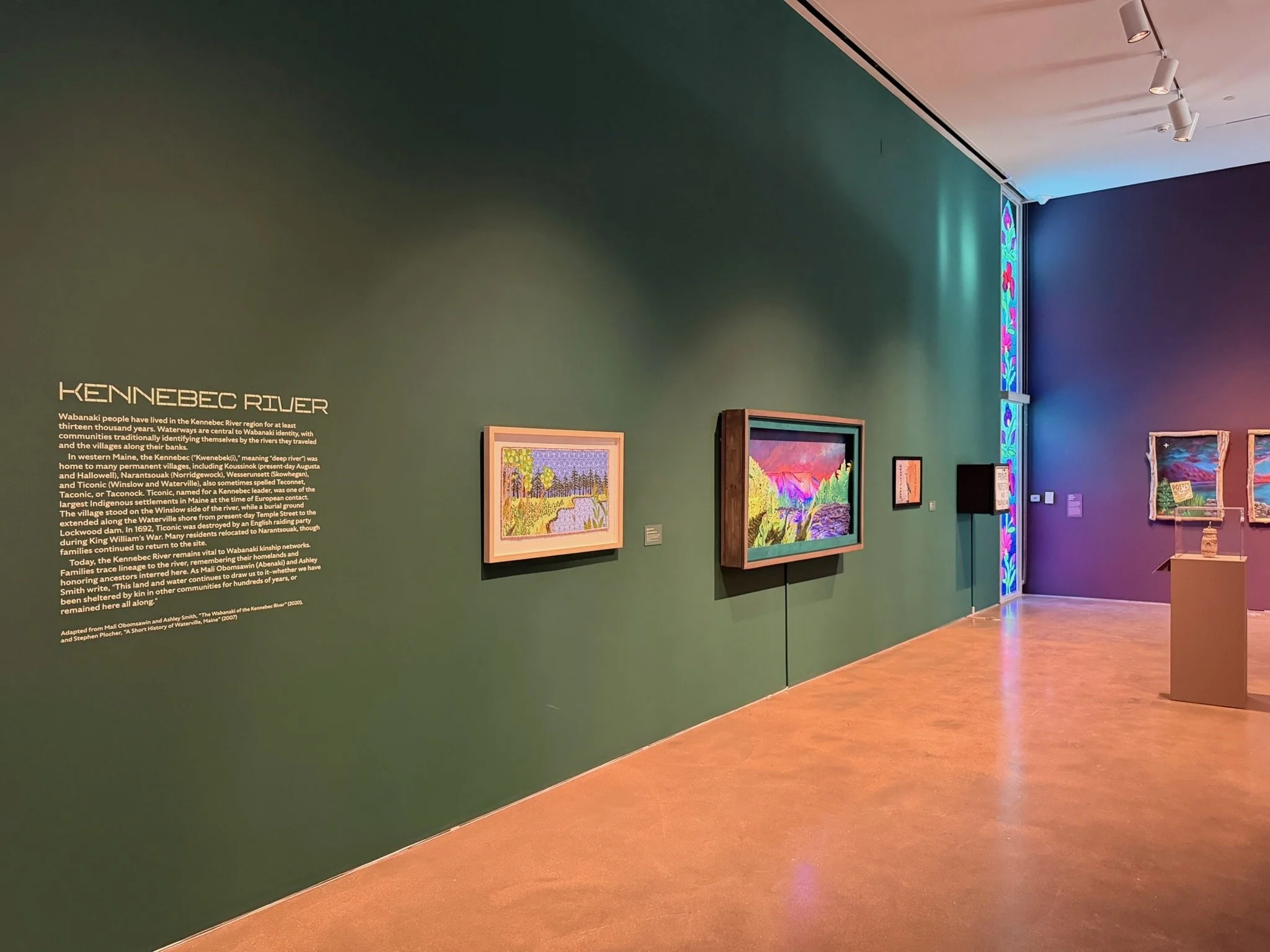 Gallery wall display of paintings and a text panel about the Kennebec River in a museum setting.