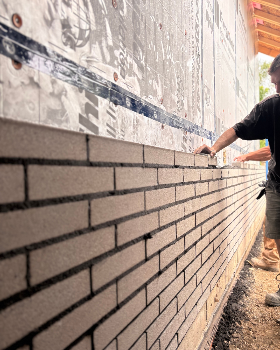 A construction worker installing bricks on a wall with insulation material overhead.