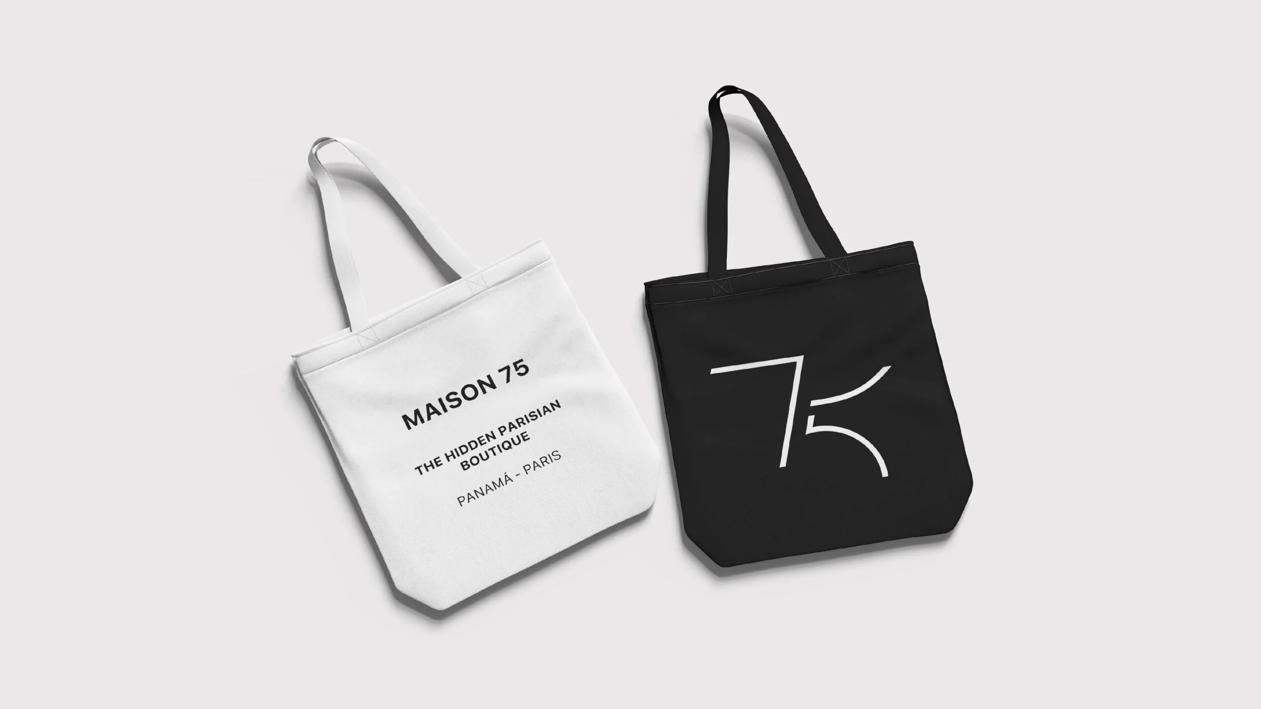 Two fabric tote bags, one white with black text and one black with a white logo, lying on a plain light gray surface.