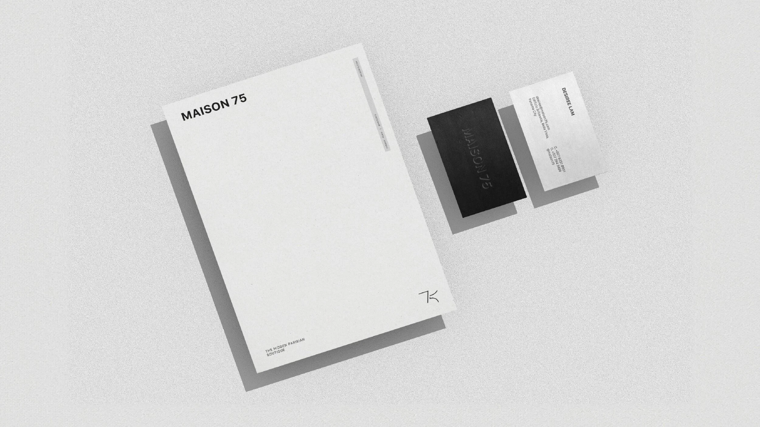 A white paper booklet titled 'MAISON 75' with minimalist black typography, and several overlapping business cards or flyers with black and white designs, placed on a light gray surface.