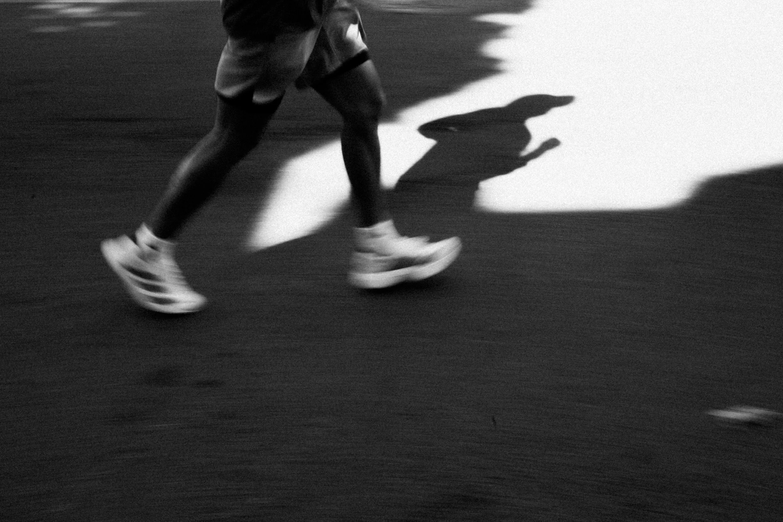 A person walking or running in motion, with a shadow cast on the ground, in black and white.