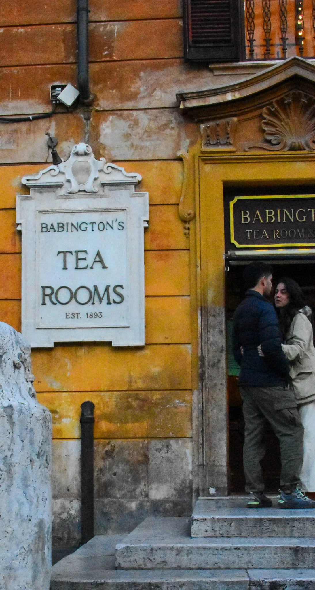A sign outside Babington's Tea Rooms established in 1893, with two people talking at the entrance.