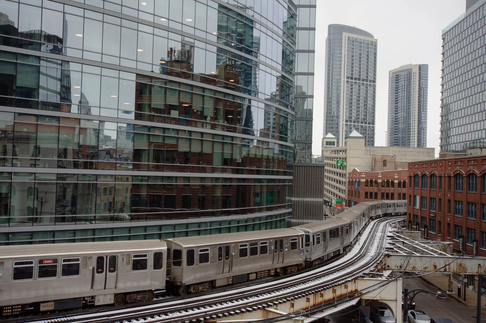 A city scene with a train on an elevated track in front of modern glass buildings and skyscrapers.