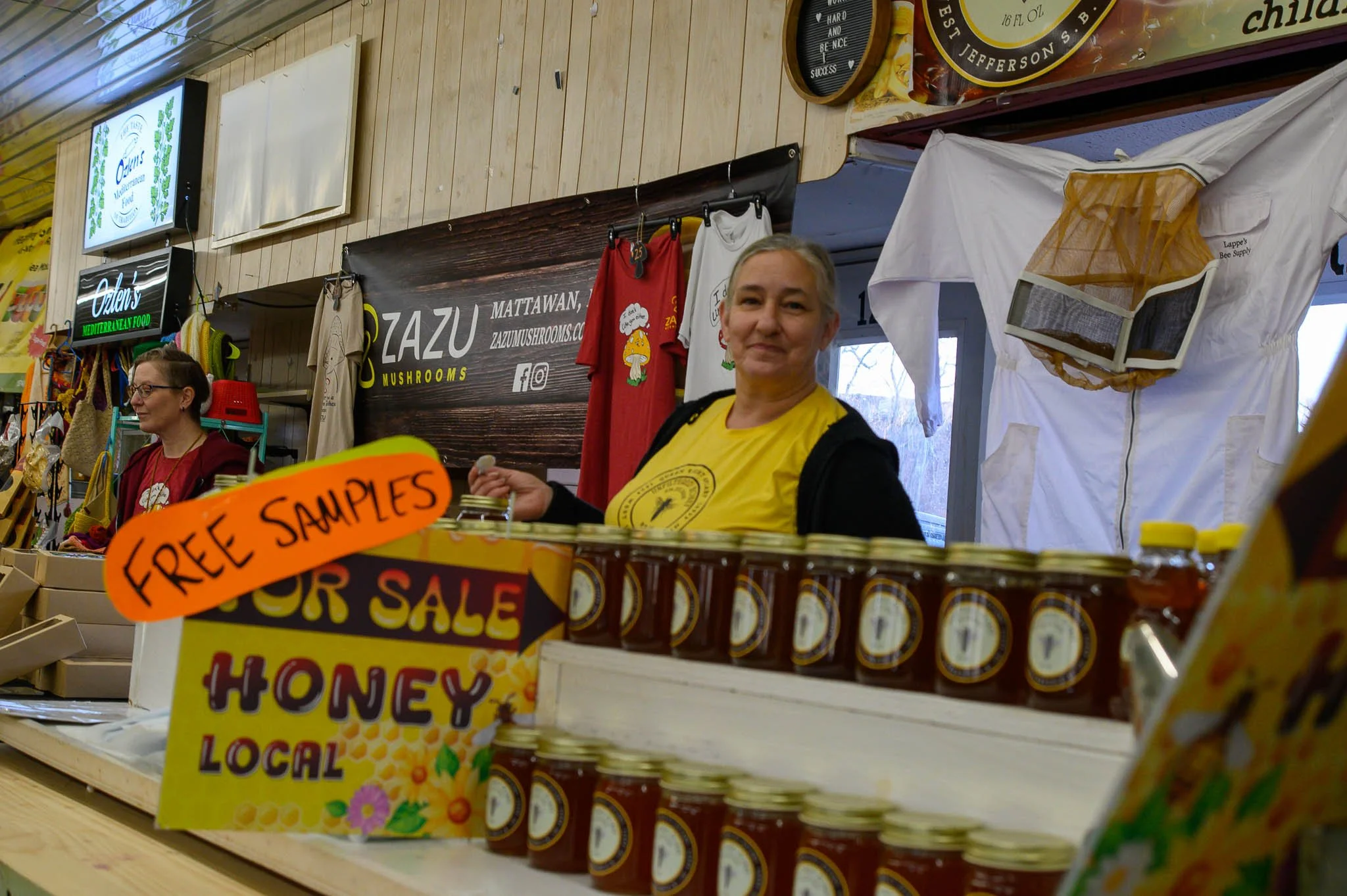 Woman at a honey stand with jars of honey and a sign for free samples.